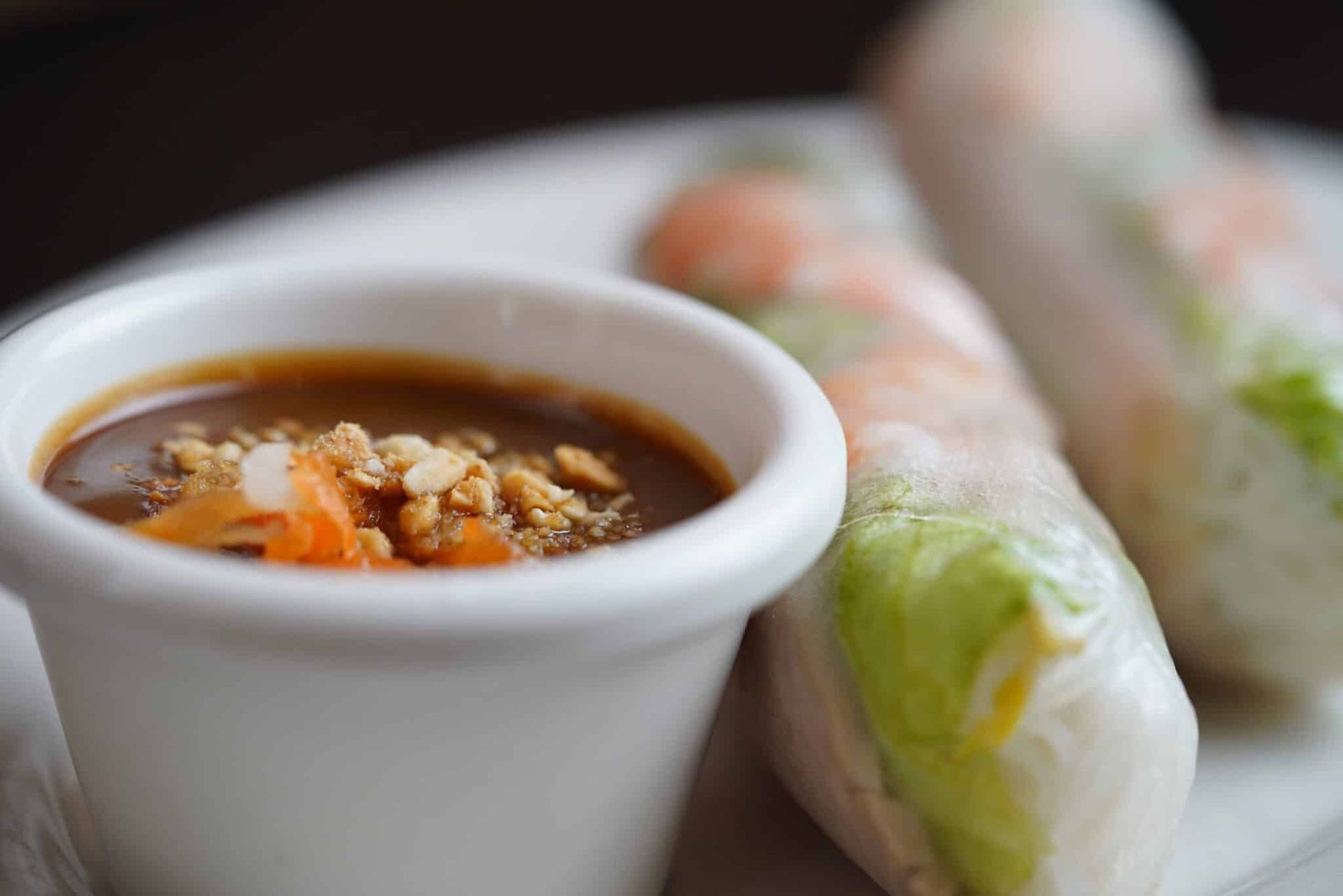Sauce cup with brown dipping sauce beside fresh spring rolls on a plate