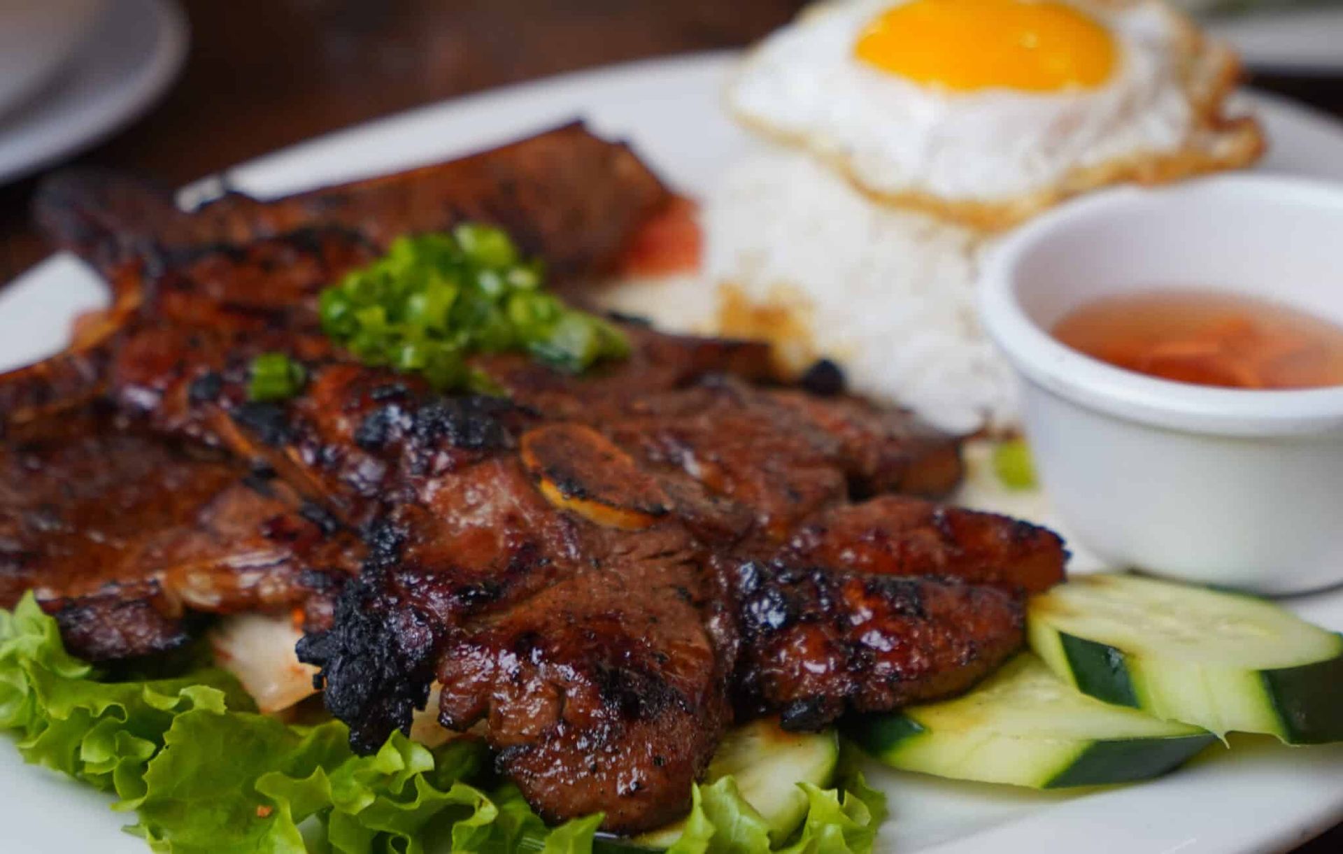 Grilled meat with rice, cucumber slices, lettuce, and dipping sauce on a plate