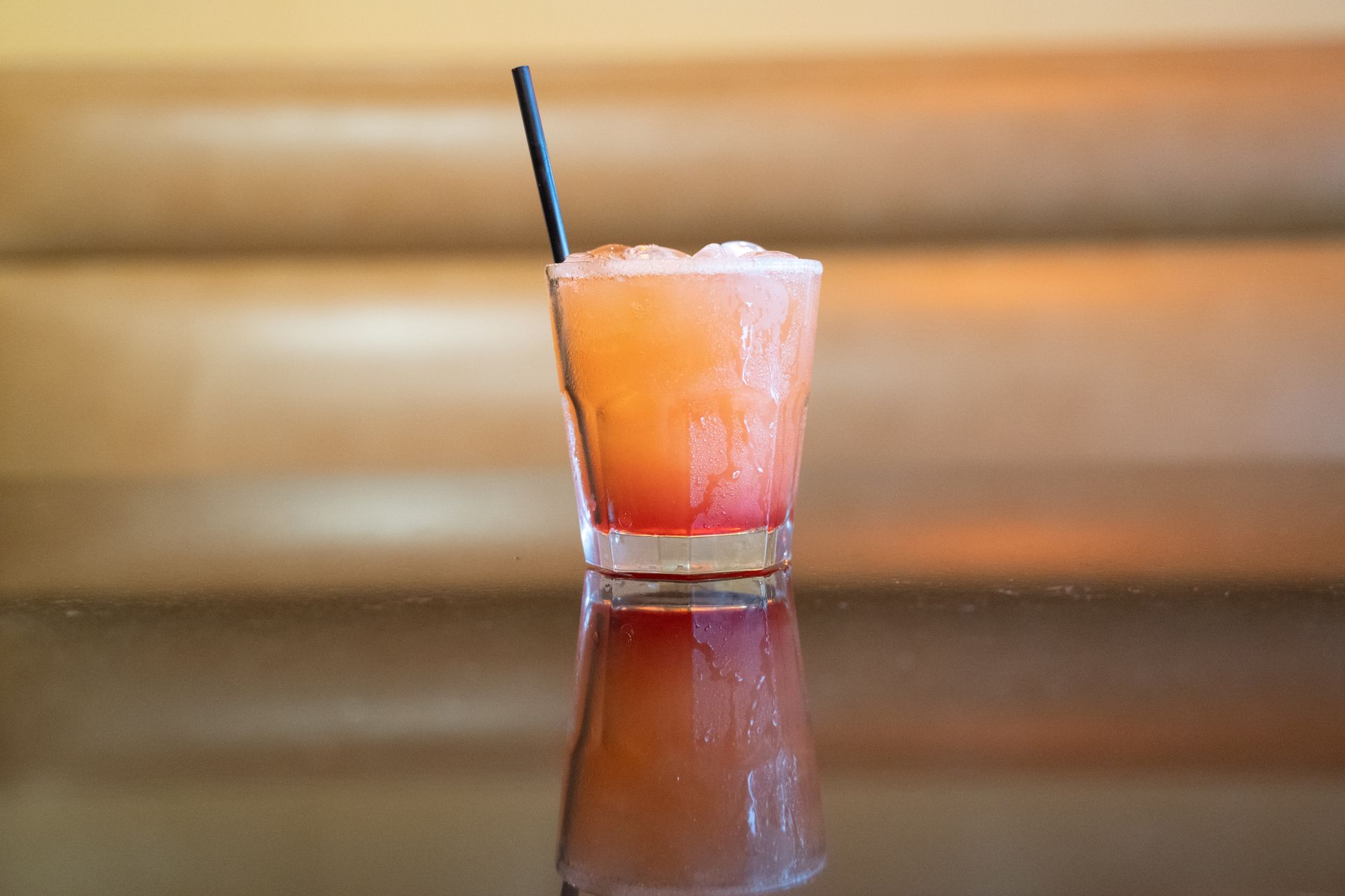 Pink cocktail in a glass with a black straw on a reflective table