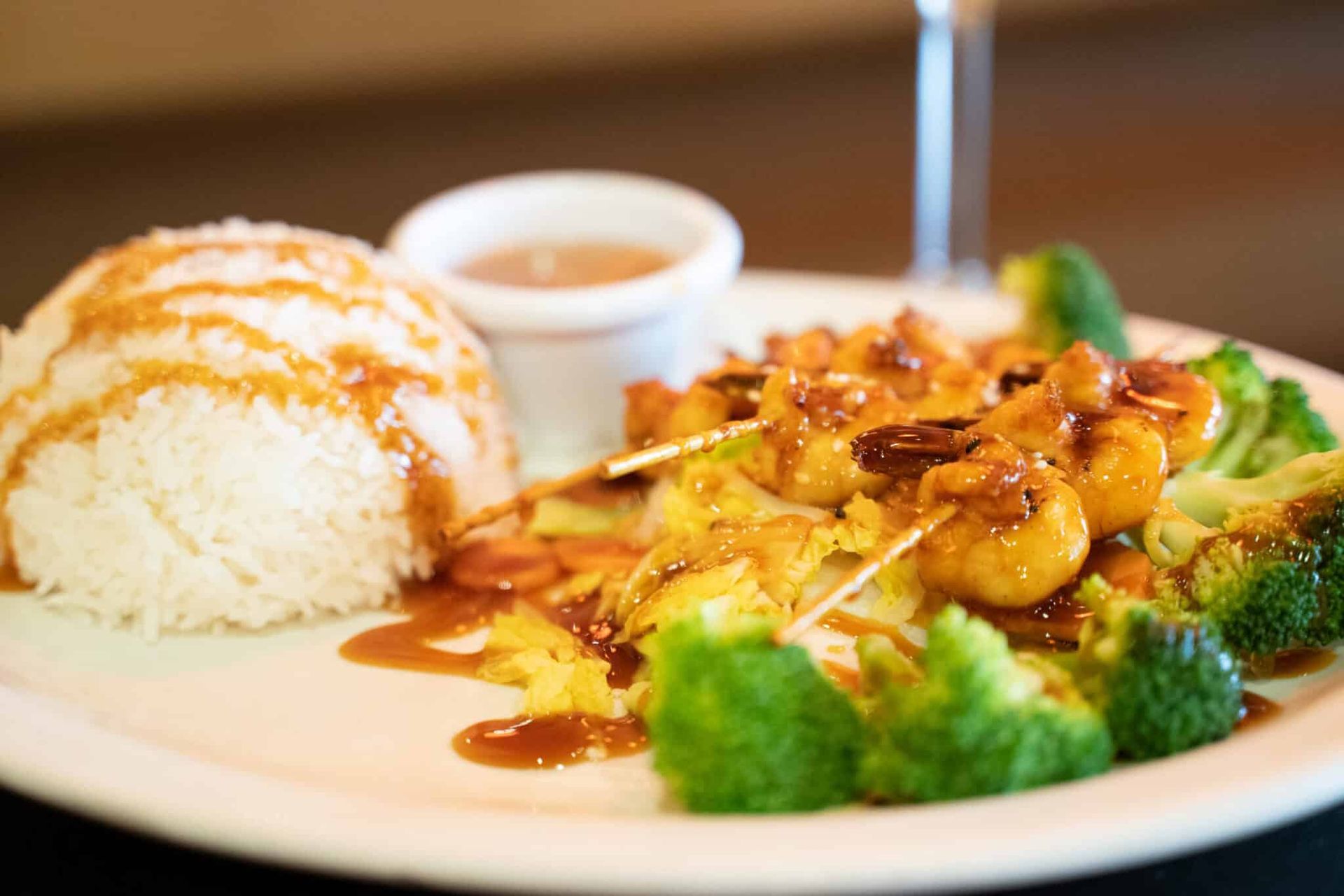 Plate with rice, sauced chicken, and broccoli, with a small dipping cup on the side