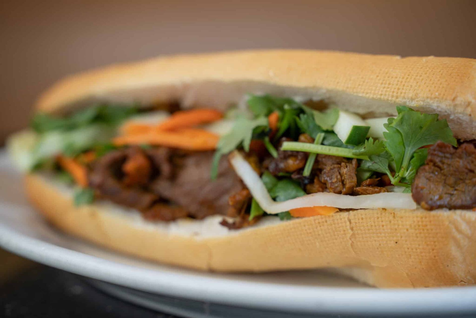 Banh mi sandwich with cilantro, pickled vegetables, and grilled meat on a plate