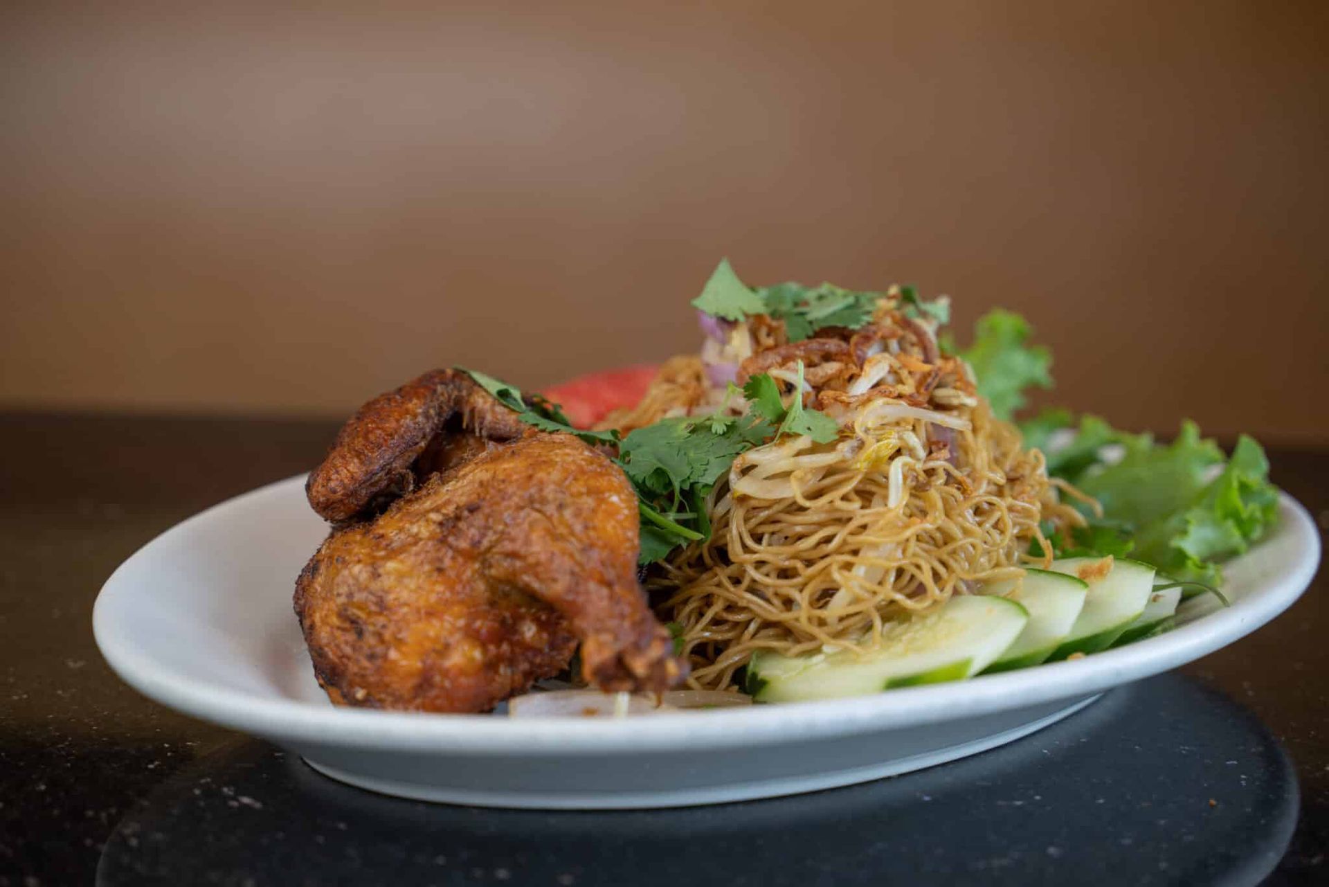 Plate of fried chicken with noodles and greens on a white dish