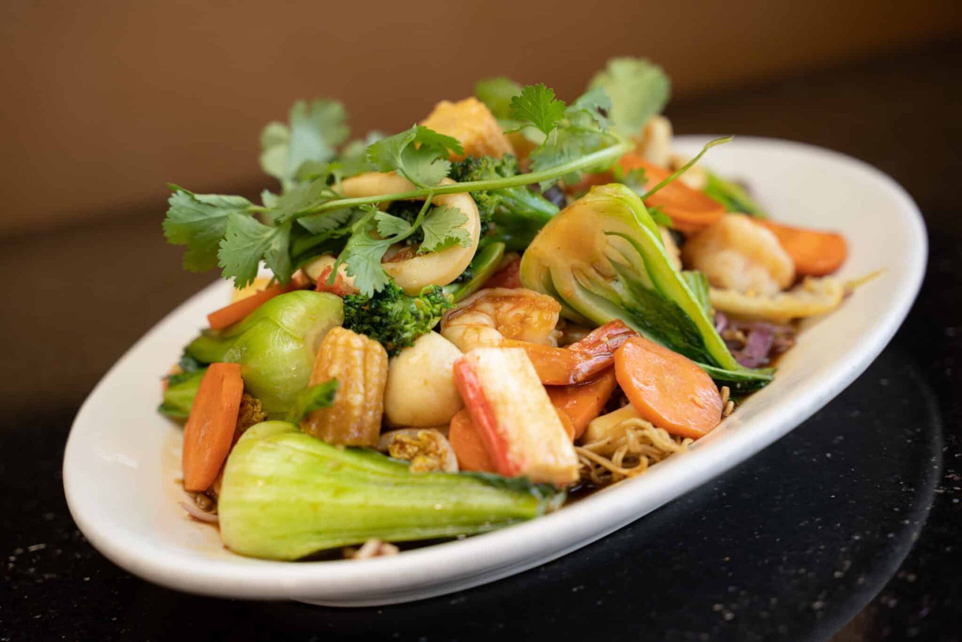 White plate of shrimp and vegetables topped with herbs, served on a dark table