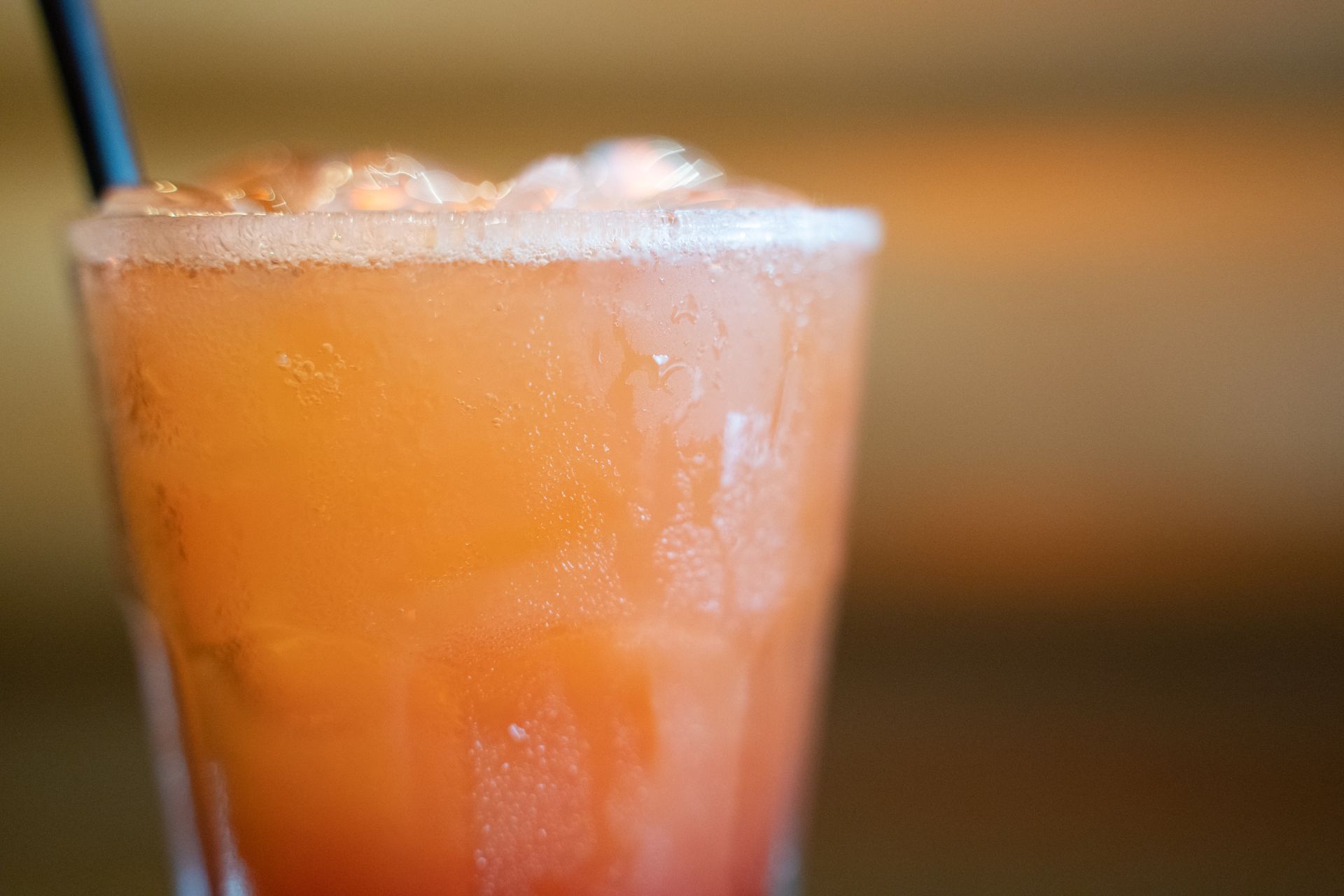 Orange cocktail in a glass with ice and a straw, against a blurred warm background