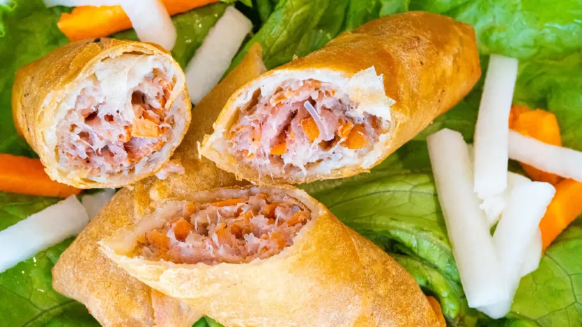 Fried spring rolls cut open on a bed of lettuce with carrot and cucumber sticks