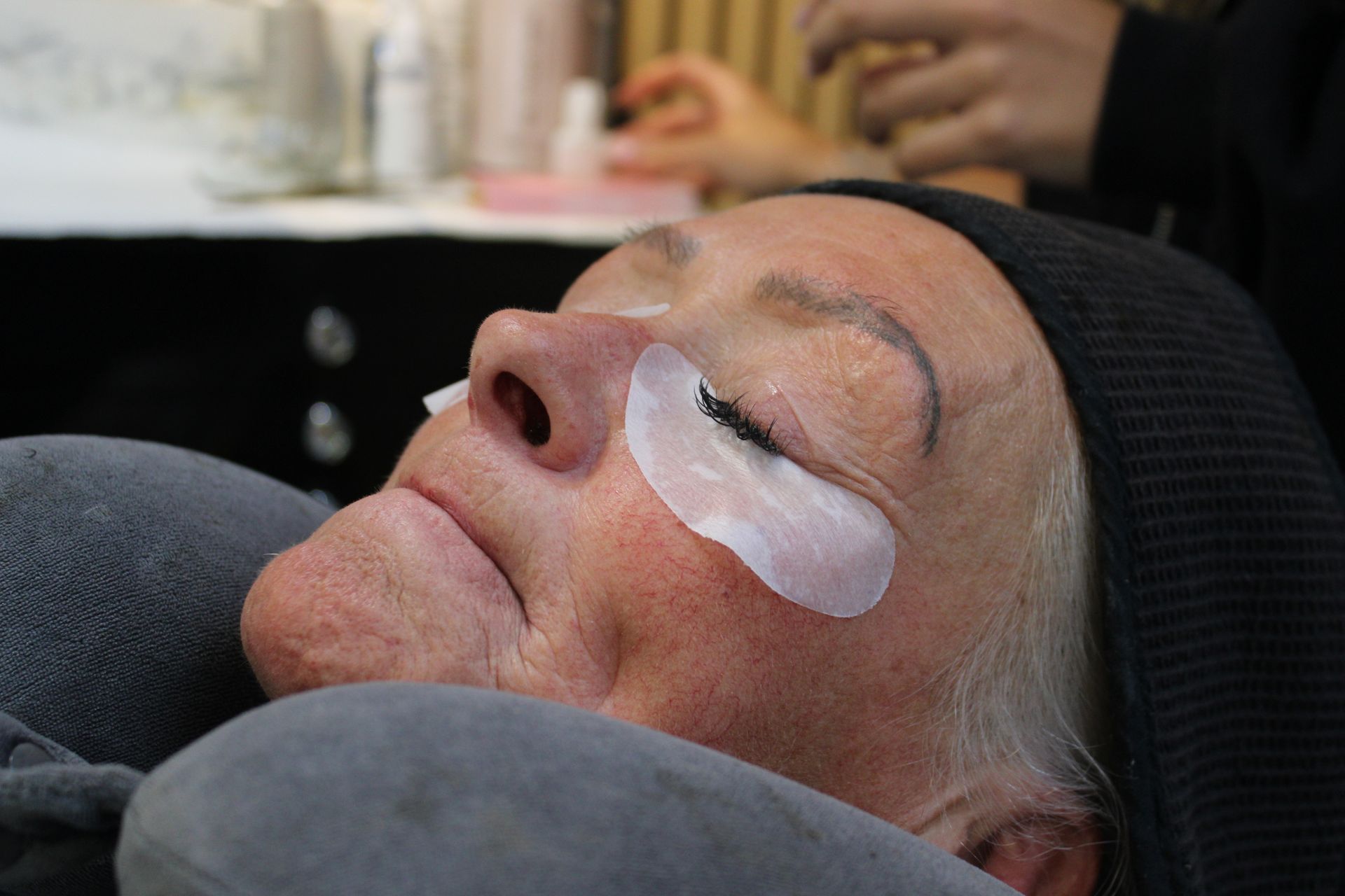Close-up of a client’s closed eye with dark lashes and an under-eye pad during a lash treatment