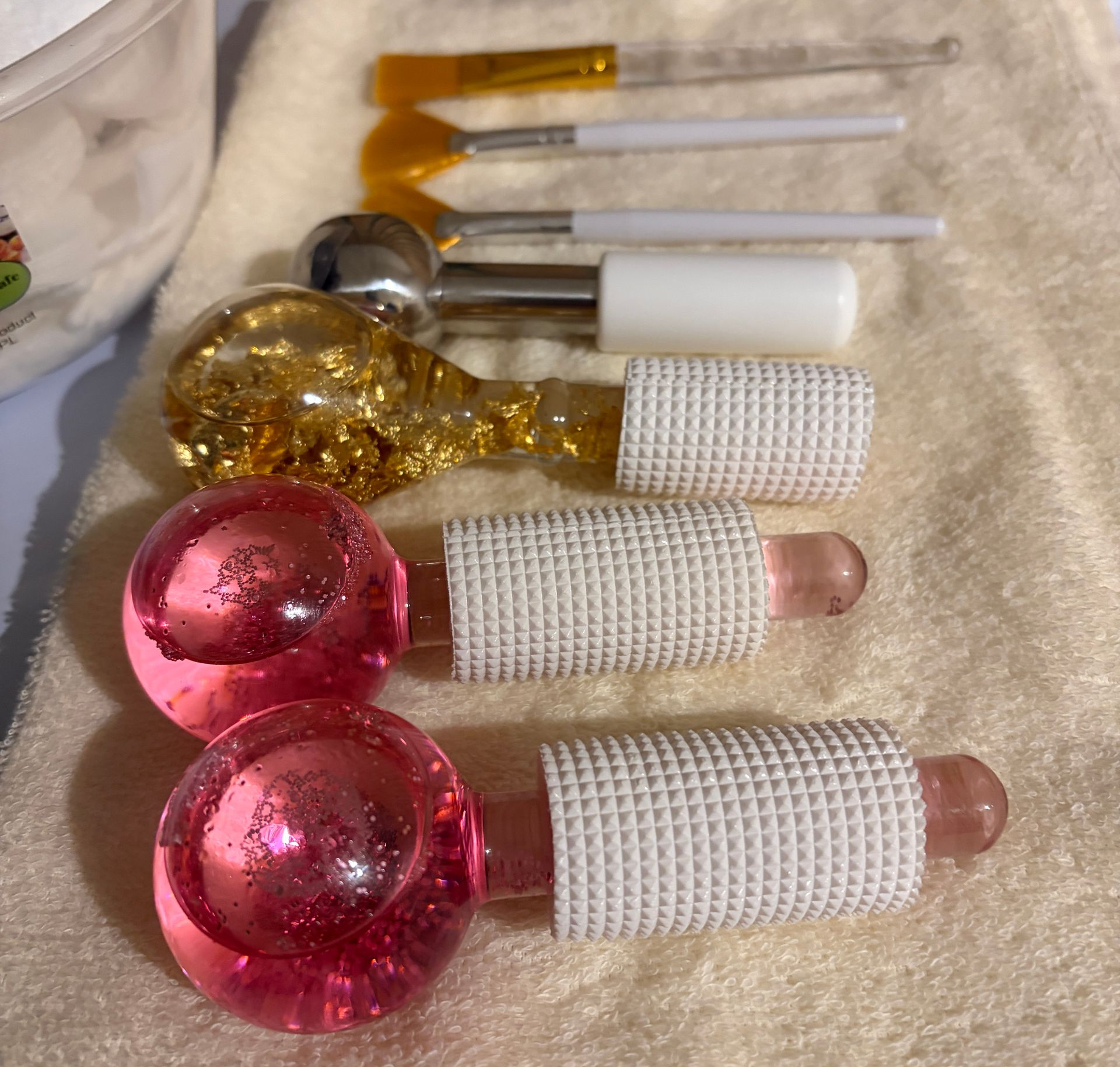 Facial brushes and pink and gold cooling globes laid out on a white towel for a facial treatment