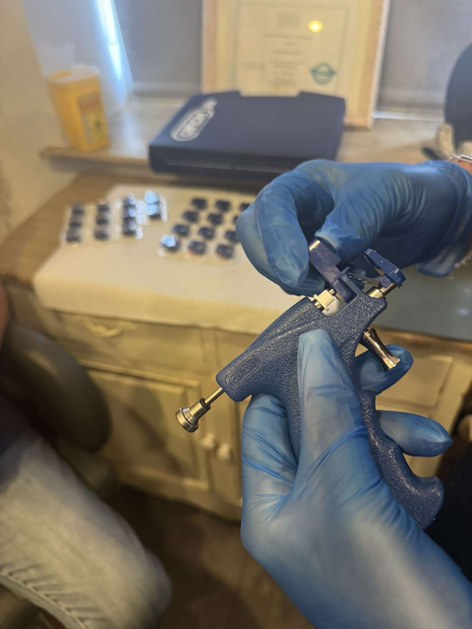 Therapist in blue gloves holding an ear piercing gun loaded with a sterile stud at Claws Nail and Beauty Daventry