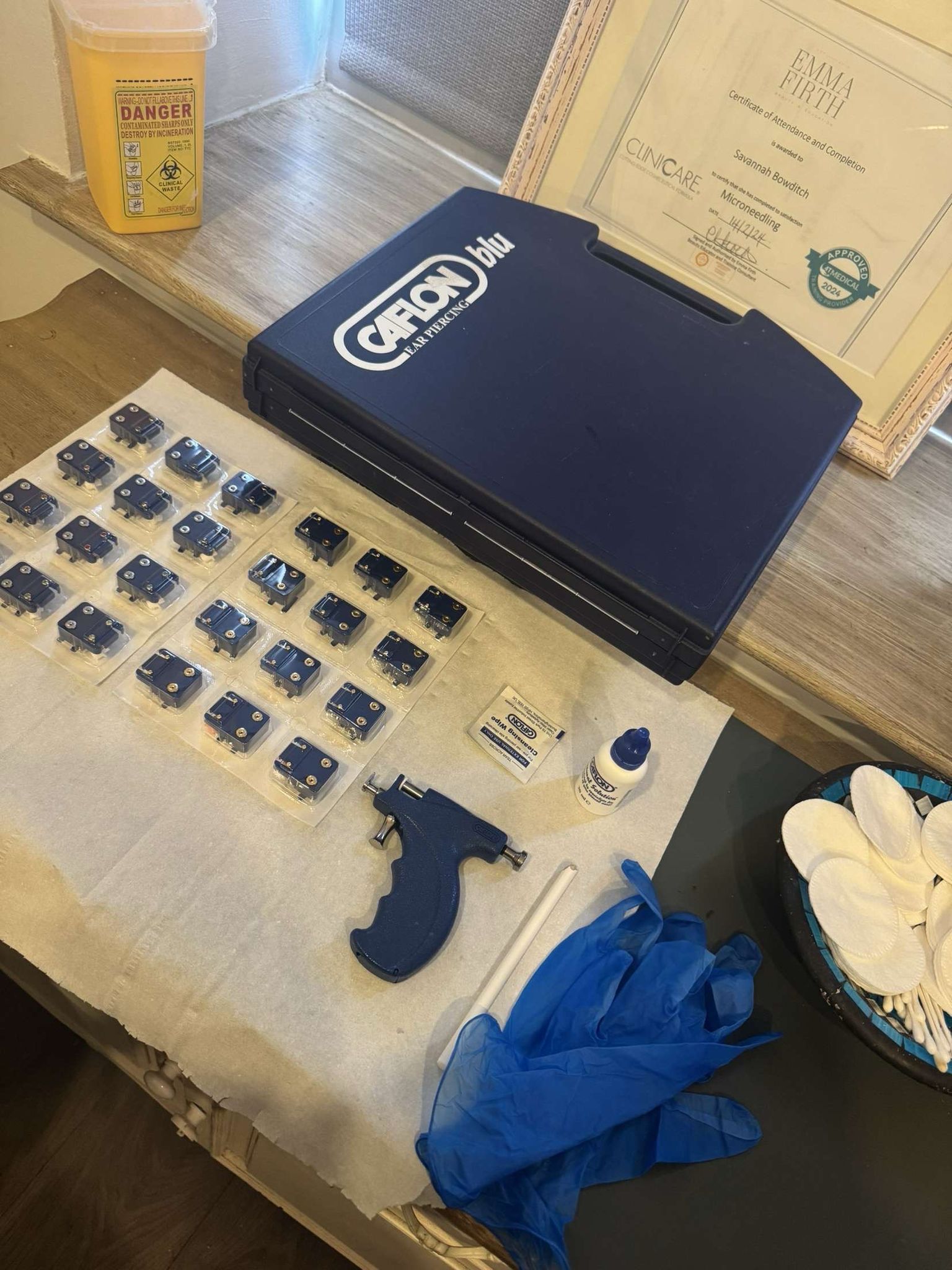 Ear piercing kit with the gun, rows of sterile packaged studs, gloves and cotton pads laid out on a tray