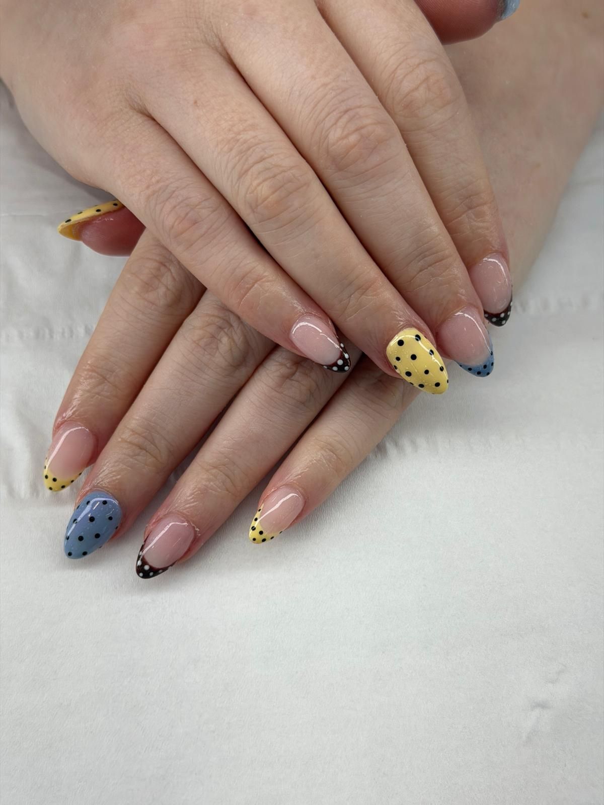 Almond nails with a nude base and yellow, blue and black polka dot French tips at Claws Nail and Beauty