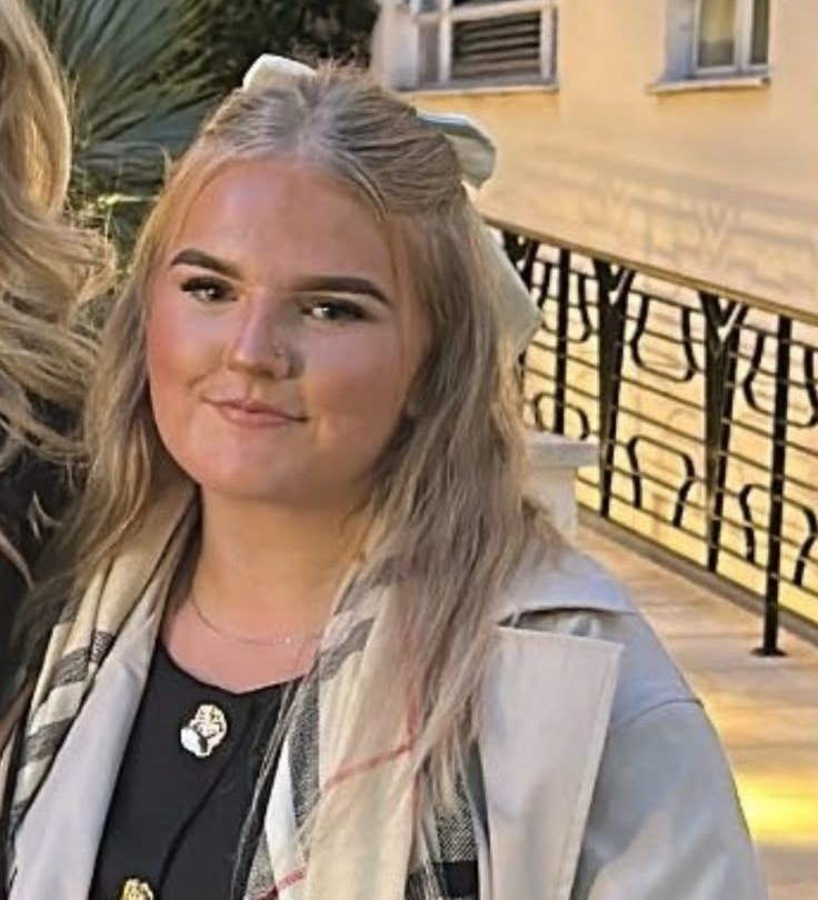 Lillie at Claws Nail and Beauty, with blonde hair, a white hair bow and a beige coat