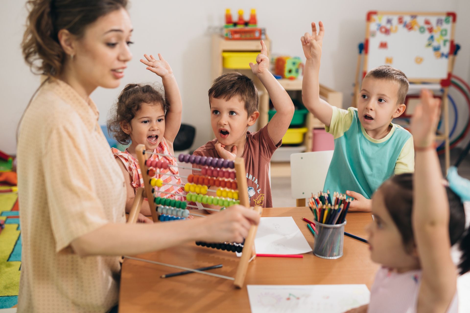 An educator with an abacus with four kids holding up their hands at a kindergarten table. An educator with an abacus with four kids holding up their hands at a kindergarten table.