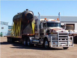 A large, cylindrical tank secured on a flatbed trailer, pulled by a semi-truck on a sunny day.