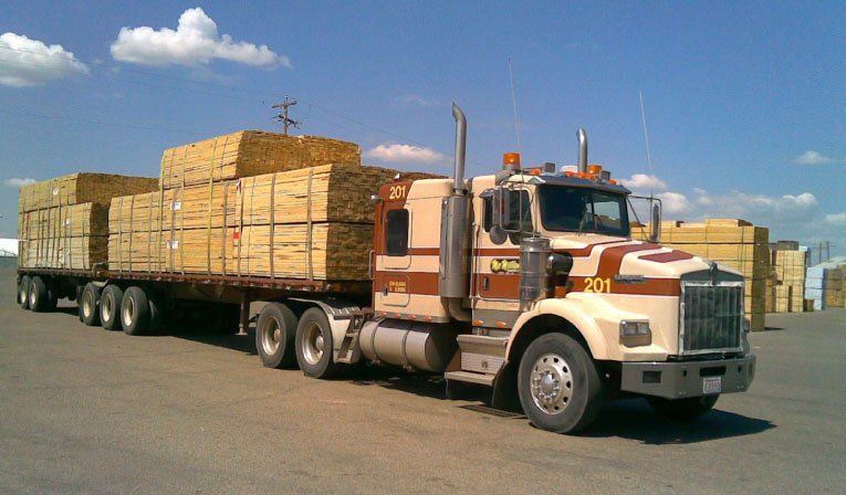 Tan semi-truck loaded with lumber on a sunny day at a lumberyard.