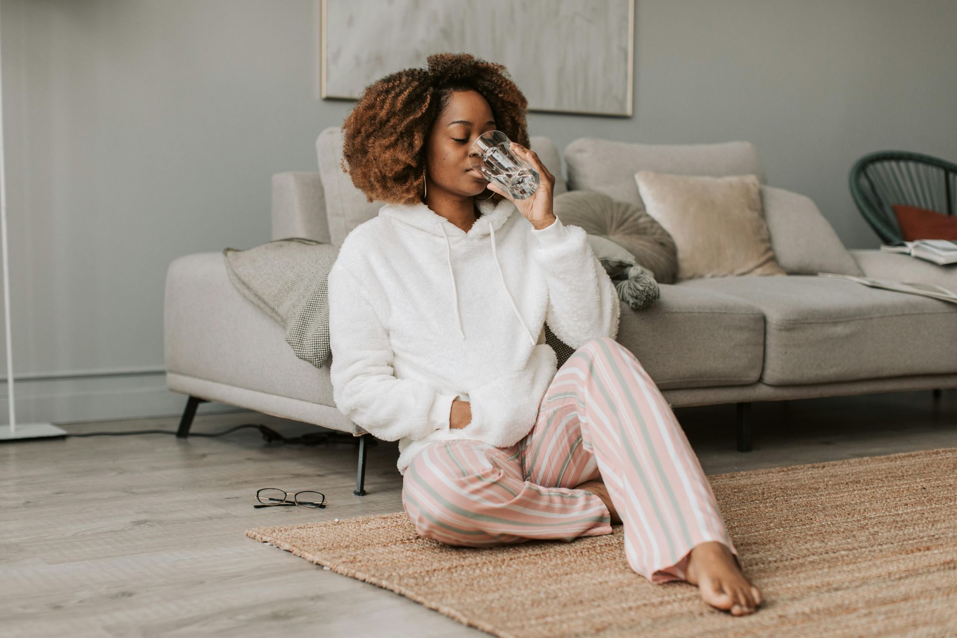Woman relaxing at home and sipping water to stay hydrated after a wellness session at Detoxity Holistic MediSpa in Texas