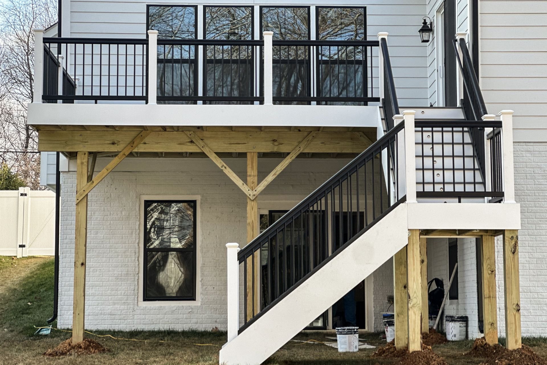 Backyard deck with black railings and white stairs, built against a white brick house, on a sunny day.