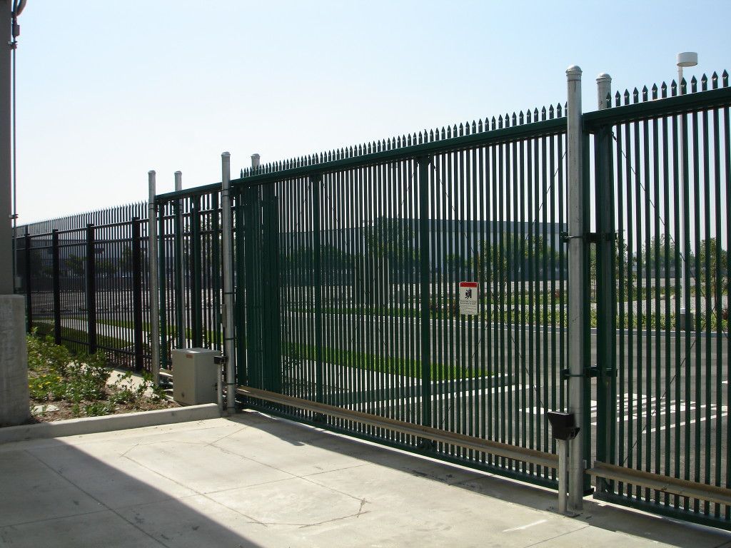 Green metal security gate, open, with a fence in the background, set on a concrete pad.