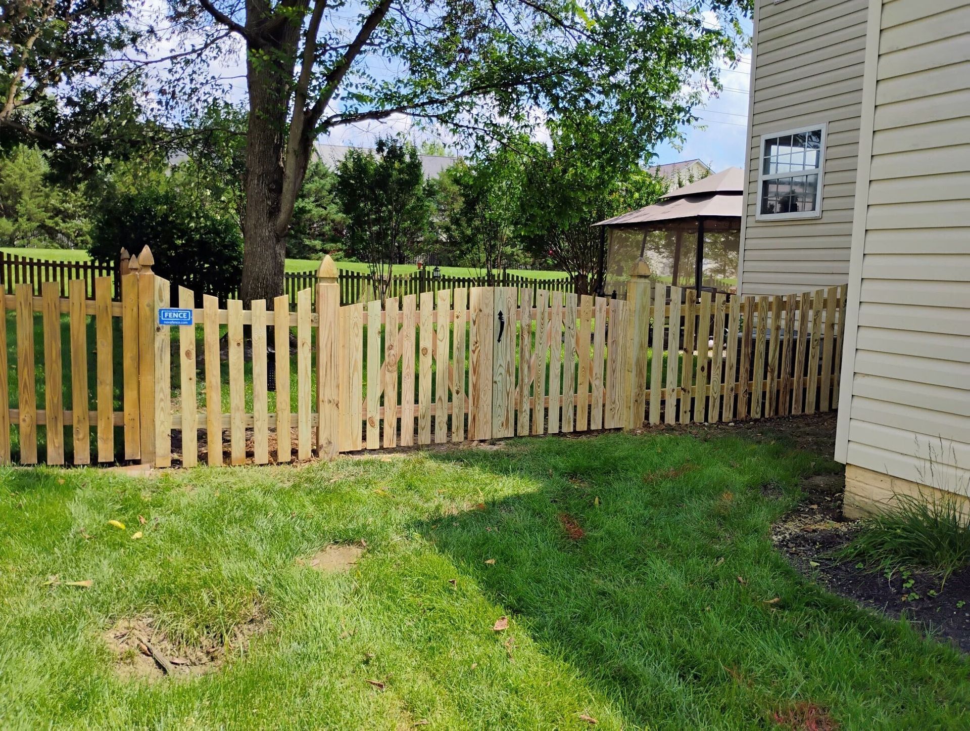 Wooden picket fence alongside a house and a grassy yard.