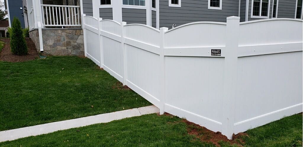 White vinyl fence enclosing a green lawn and a house.