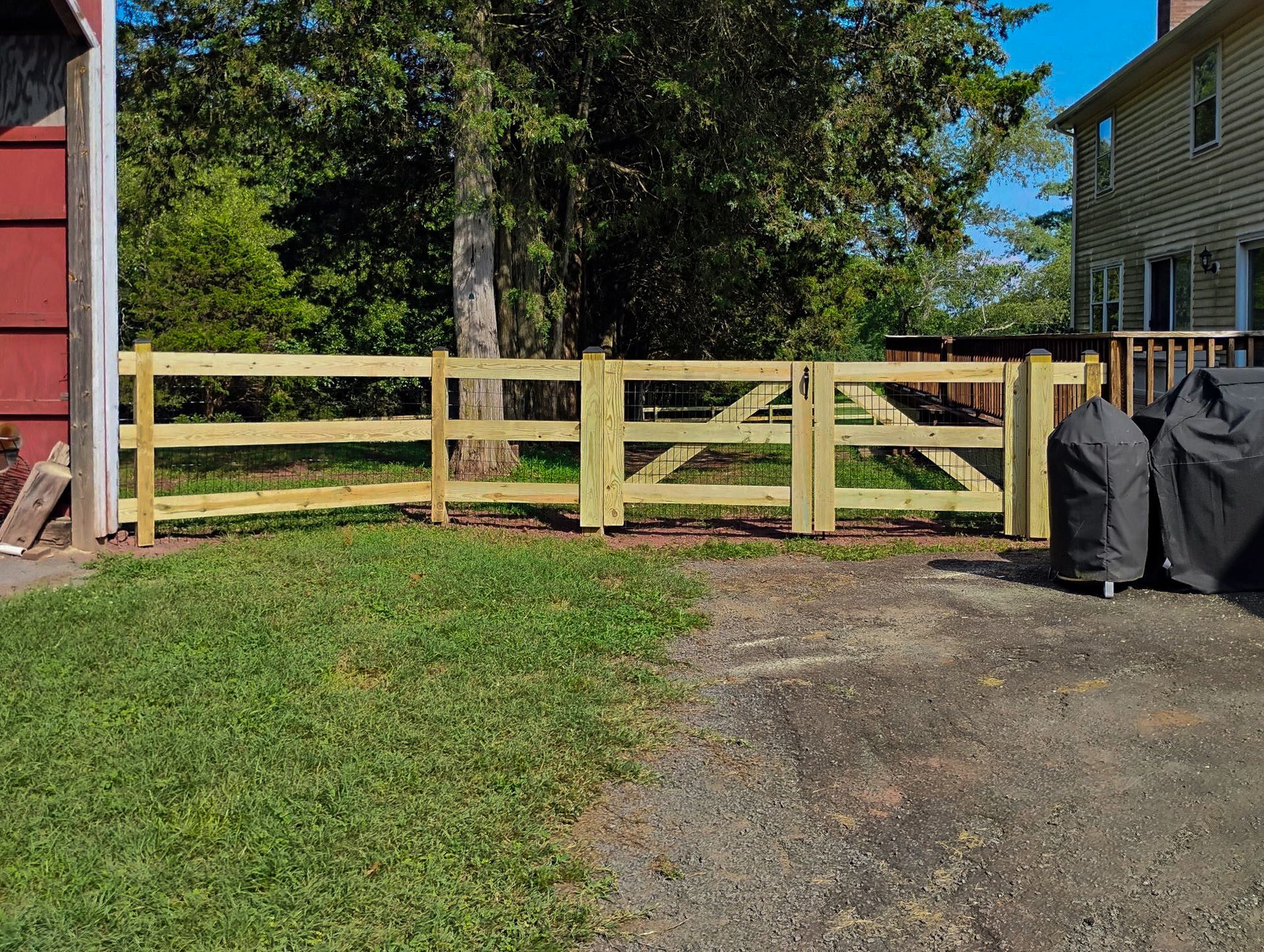 Wooden fence with gate, in front of a house, and next to a grassy lawn.