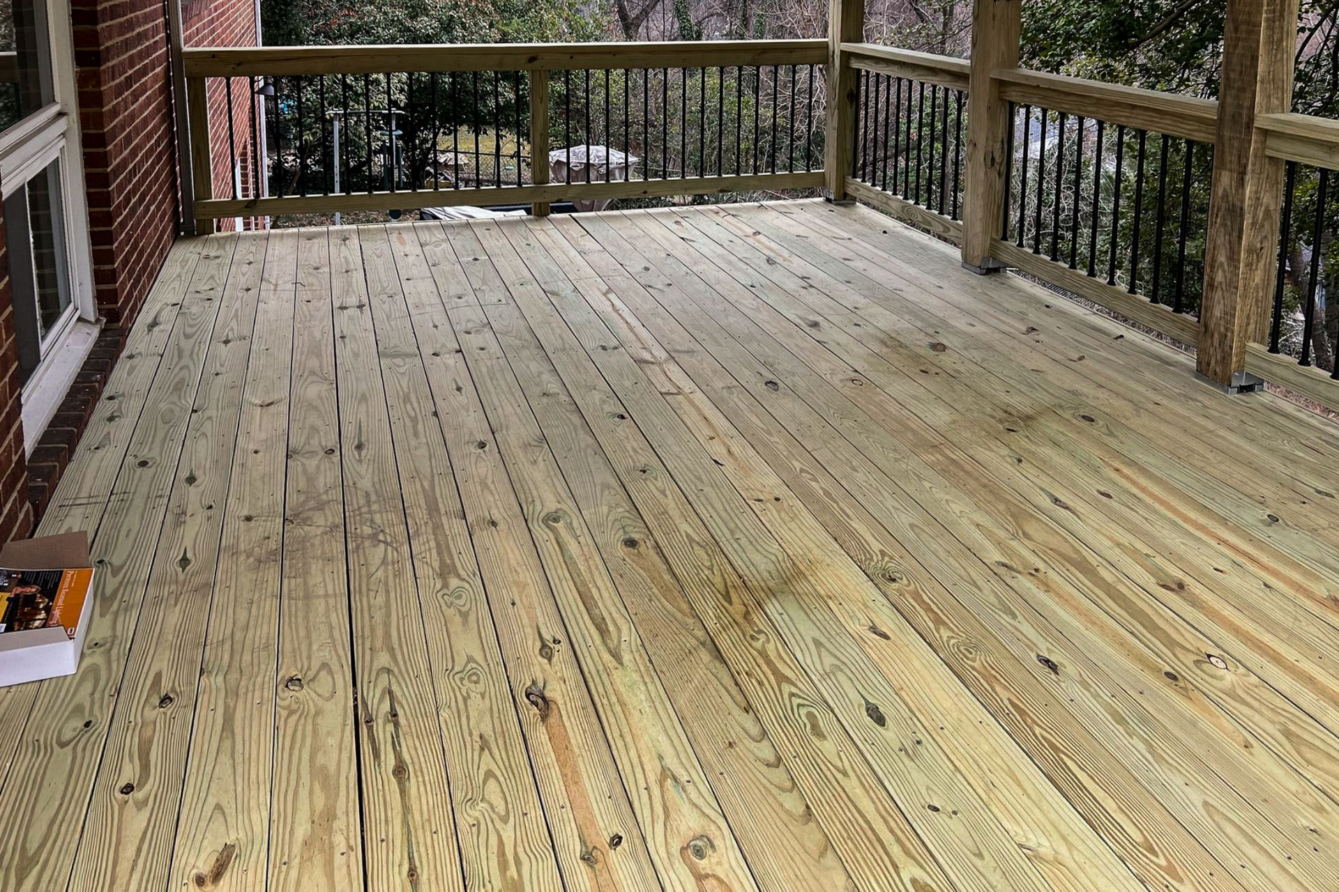 Wooden deck with railing. Light brown boards. Brick wall visible.