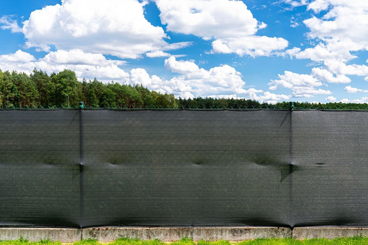 Black privacy fence with forest background and blue sky.