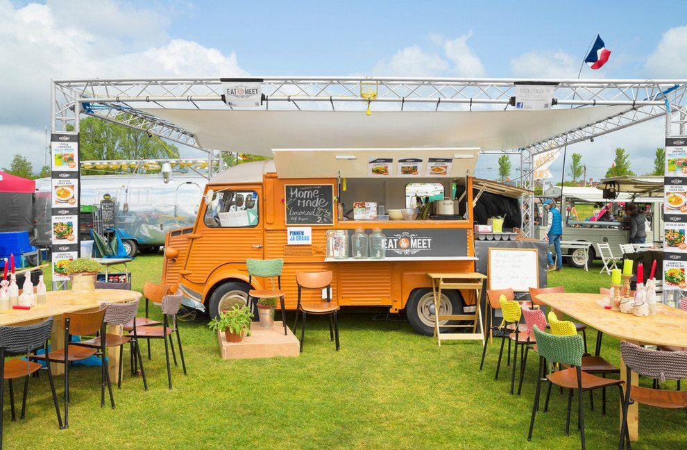 A food truck is parked in a grassy field with tables and chairs.