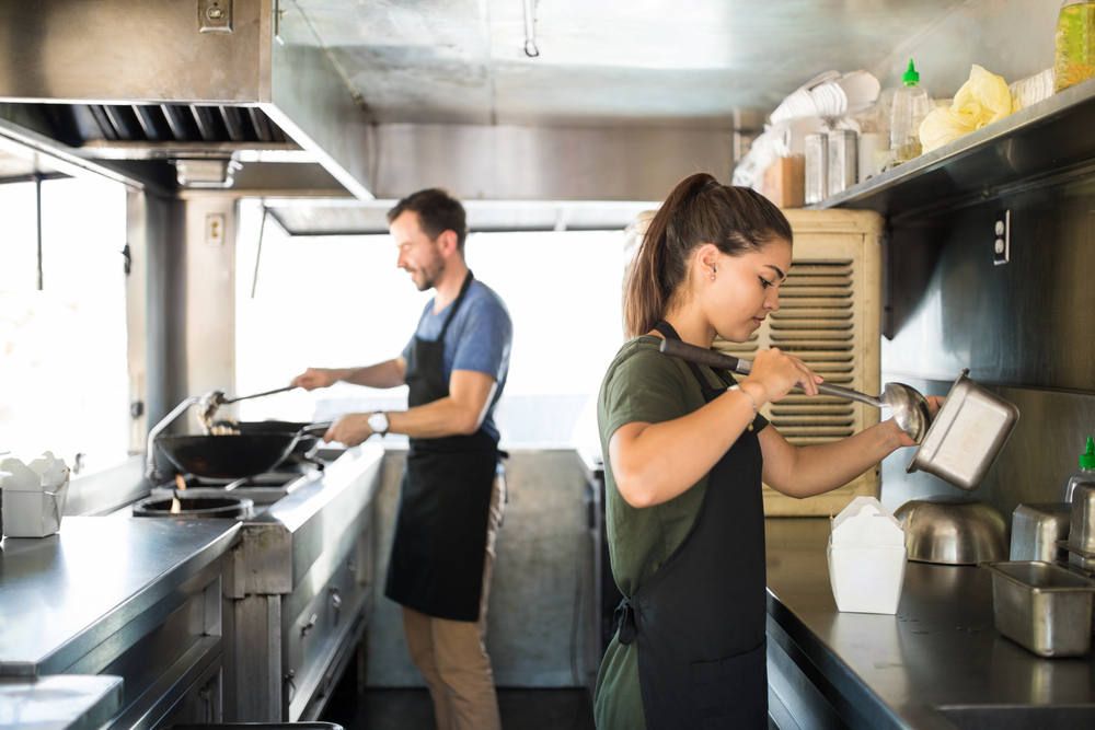 A man and a woman are cooking in a food truck kitchen.