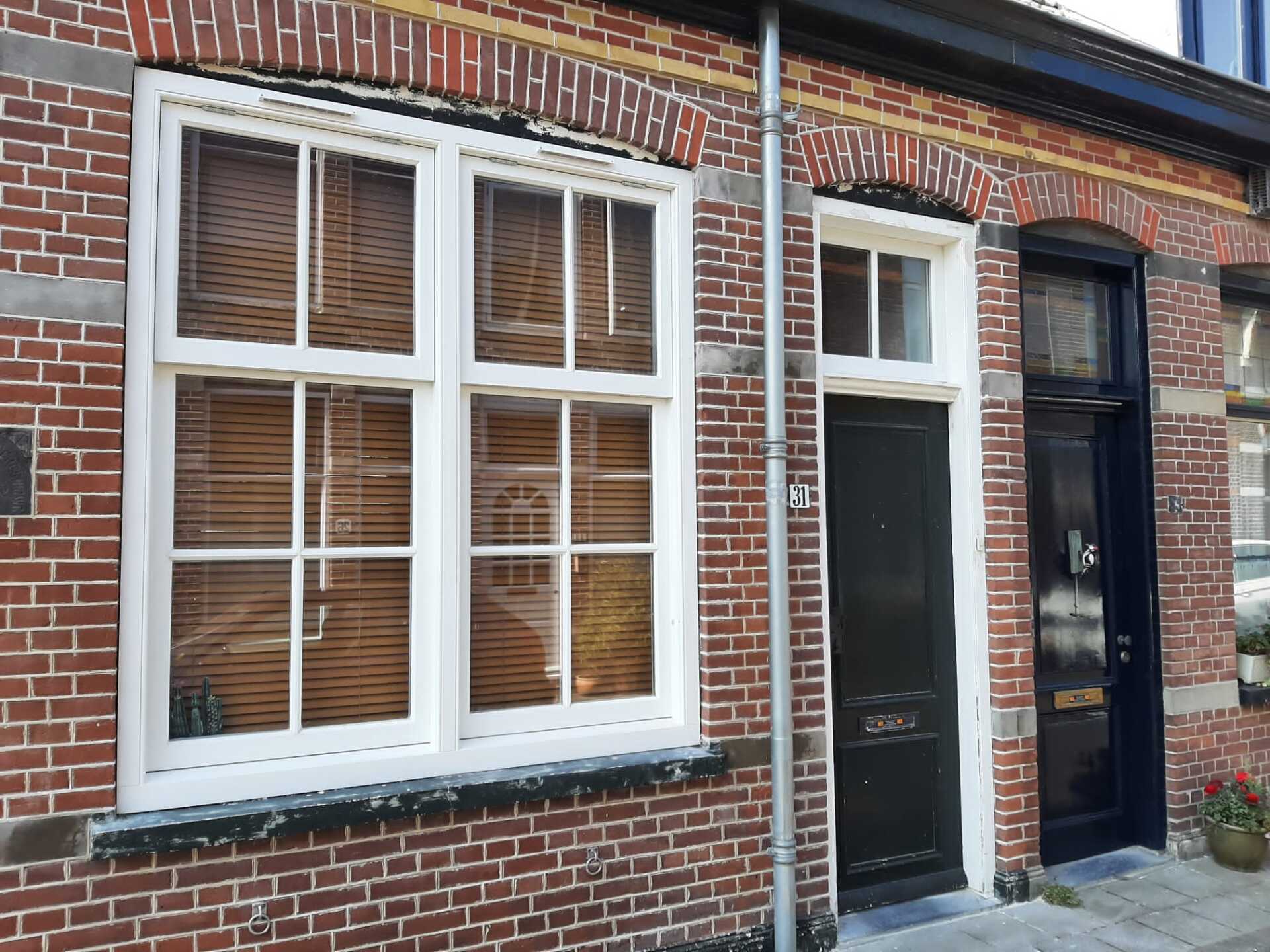 Een bakstenen winkelpand met wit omlijste ramen en een donkere deur in een smalle straat.