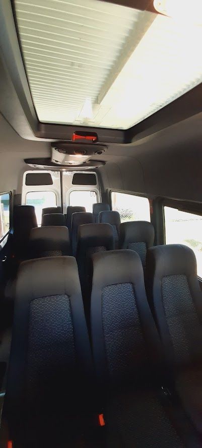 Vista interior de una camioneta de pasajeros con filas de asientos azules e iluminación superior.