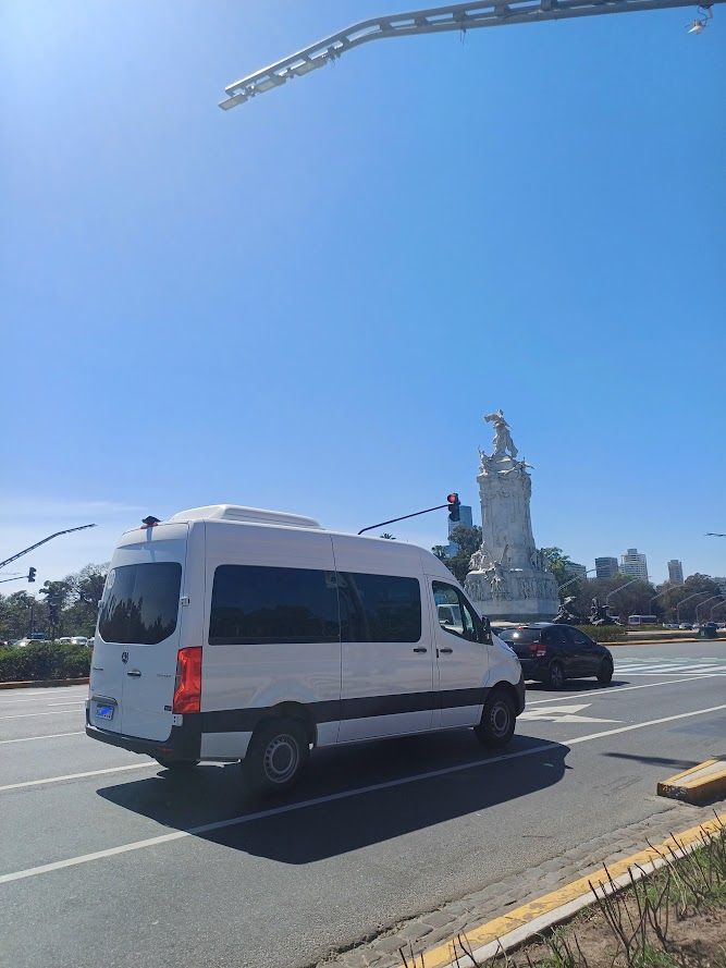 Furgoneta blanca en una carretera con una escultura al fondo bajo un cielo azul.