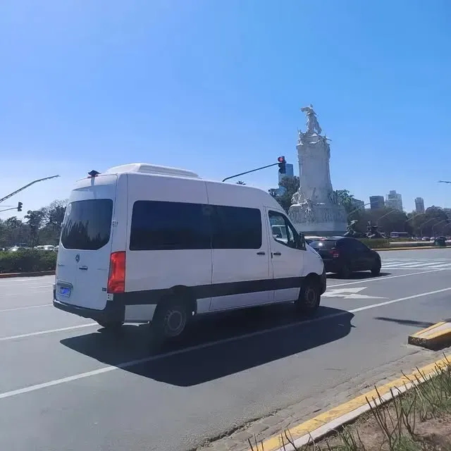 Furgoneta blanca circulando por la carretera, estatua al fondo, día soleado.