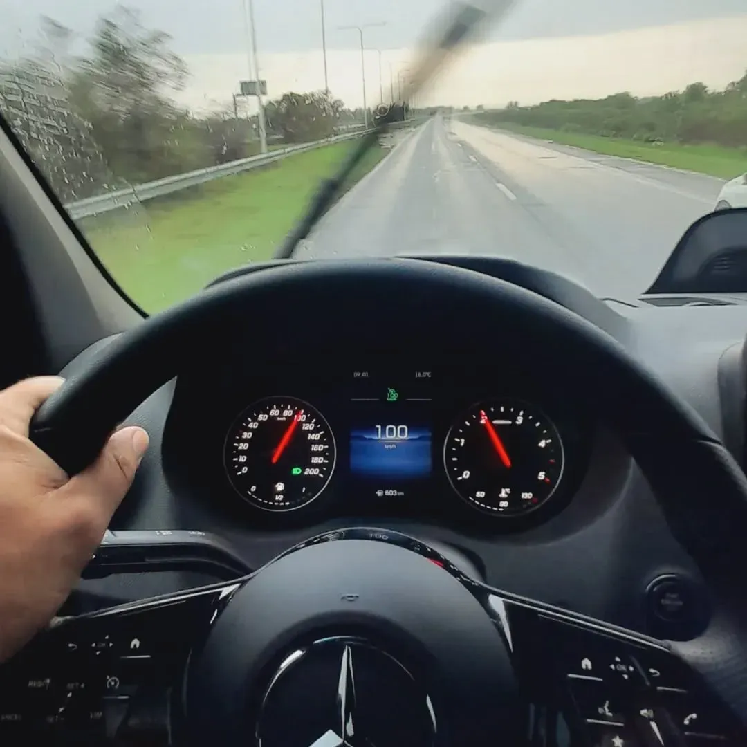 Conducir un vehículo bajo la lluvia; las manos del conductor en el volante, la autopista a lo lejos