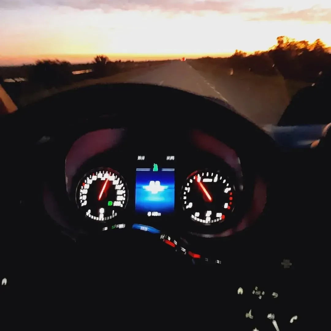 Vista del tablero de un automóvil circulando por una carretera al atardecer, con el velocímetro a 60 mph.