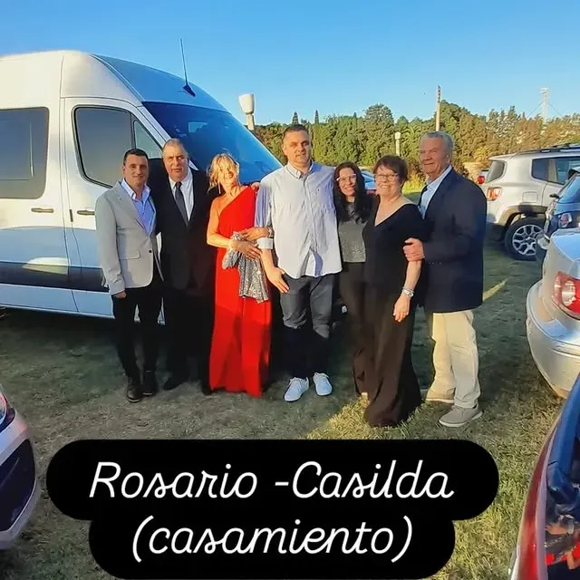 Grupo de personas vestidas formalmente posan frente a una camioneta, el texto en la parte inferior dice 