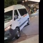 Furgoneta de pasajeros blanca estacionada en una calle por la noche, con el logotipo de la empresa en el costado.