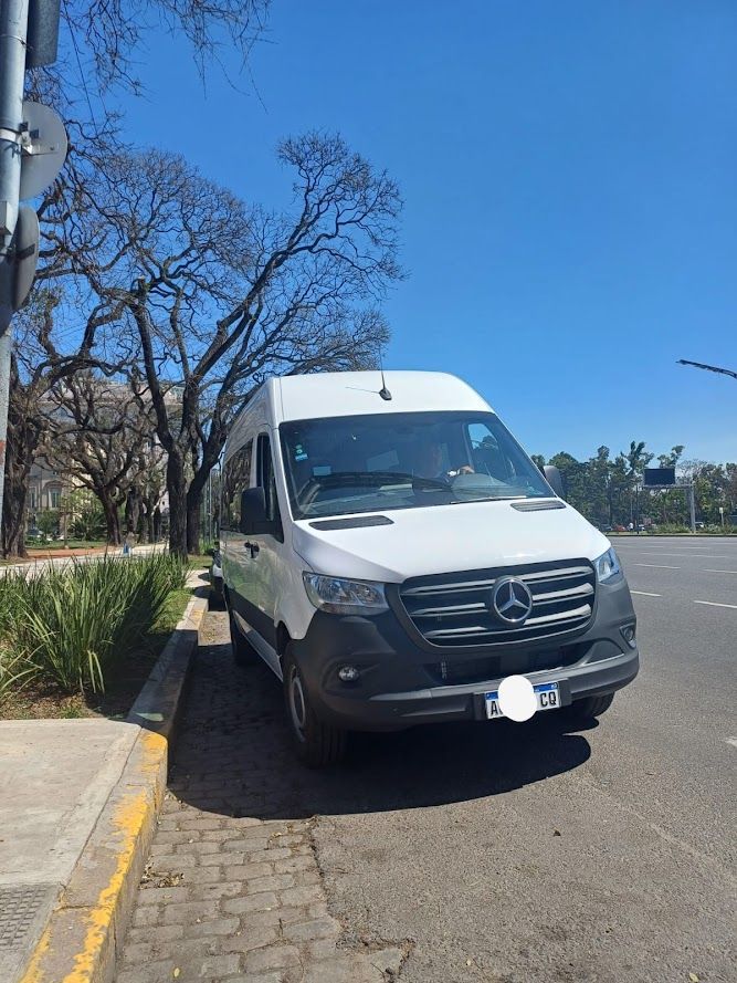 Furgoneta Mercedes-Benz blanca estacionada en una calle con árboles y un cielo azul.