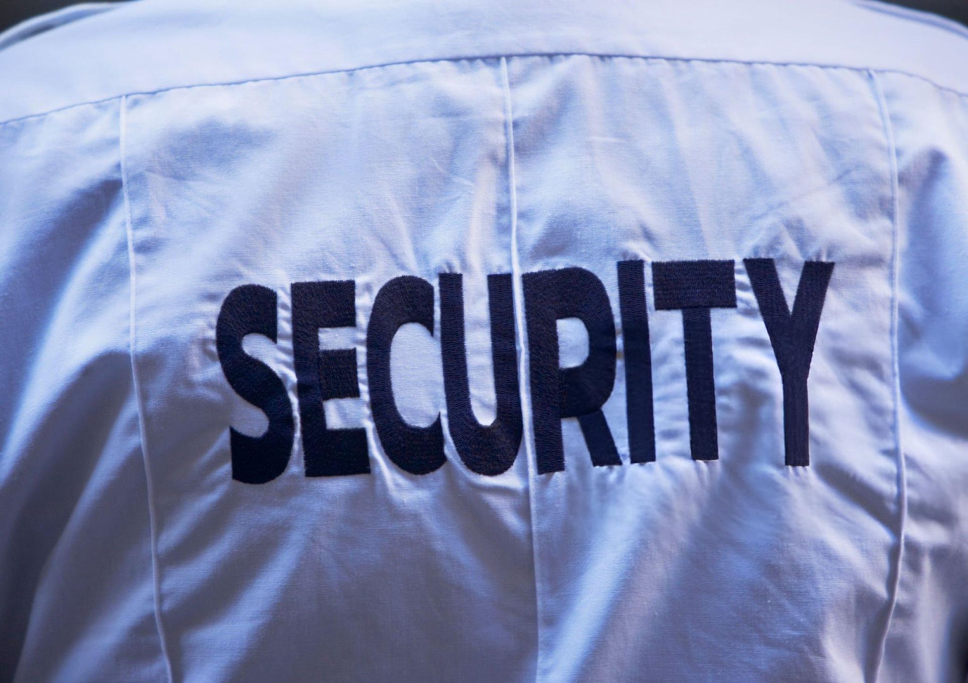 A security guard is standing in front of a door with his arms crossed.