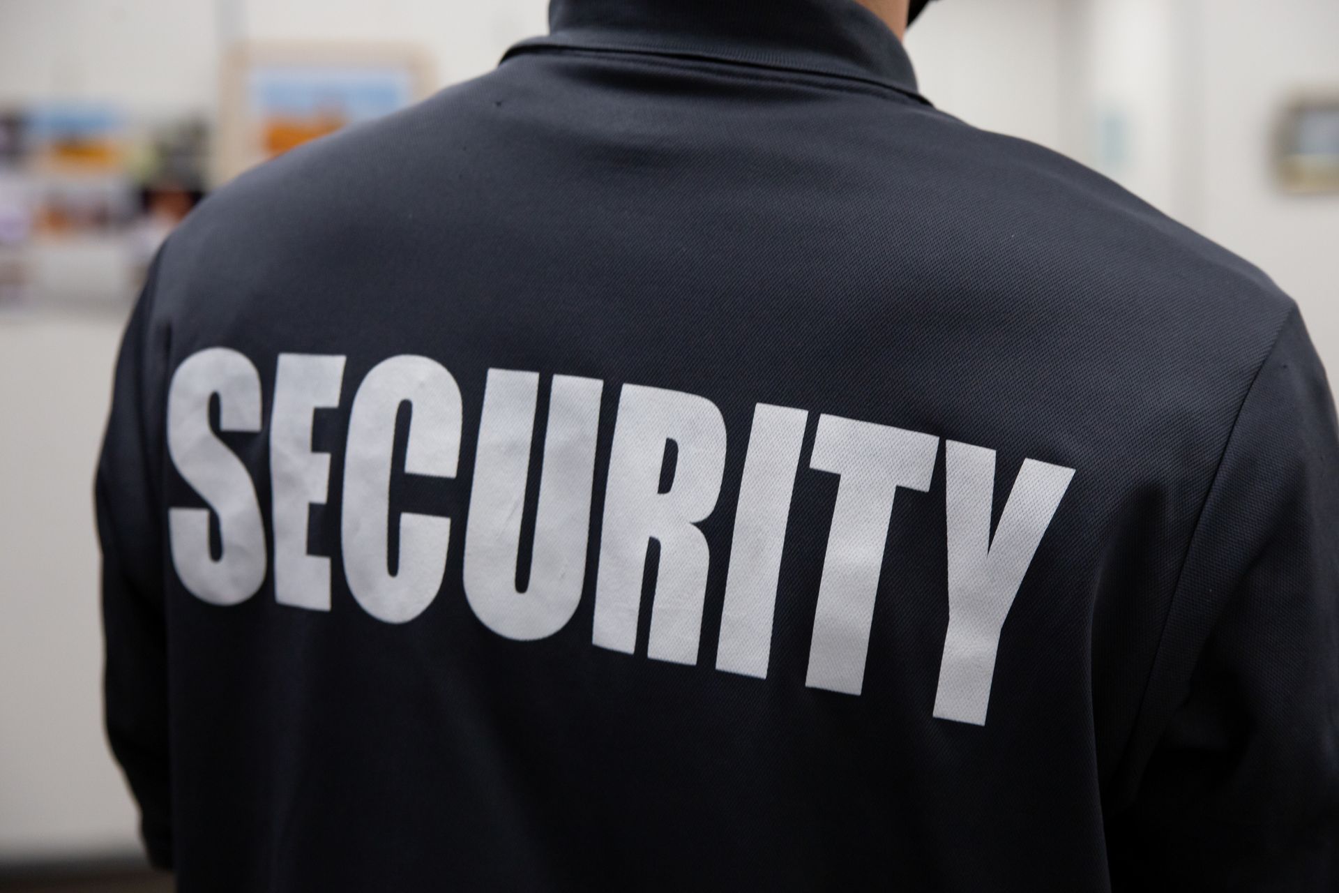 Rear view of security guard in uniform patrolling an art gallery in a commercial building.