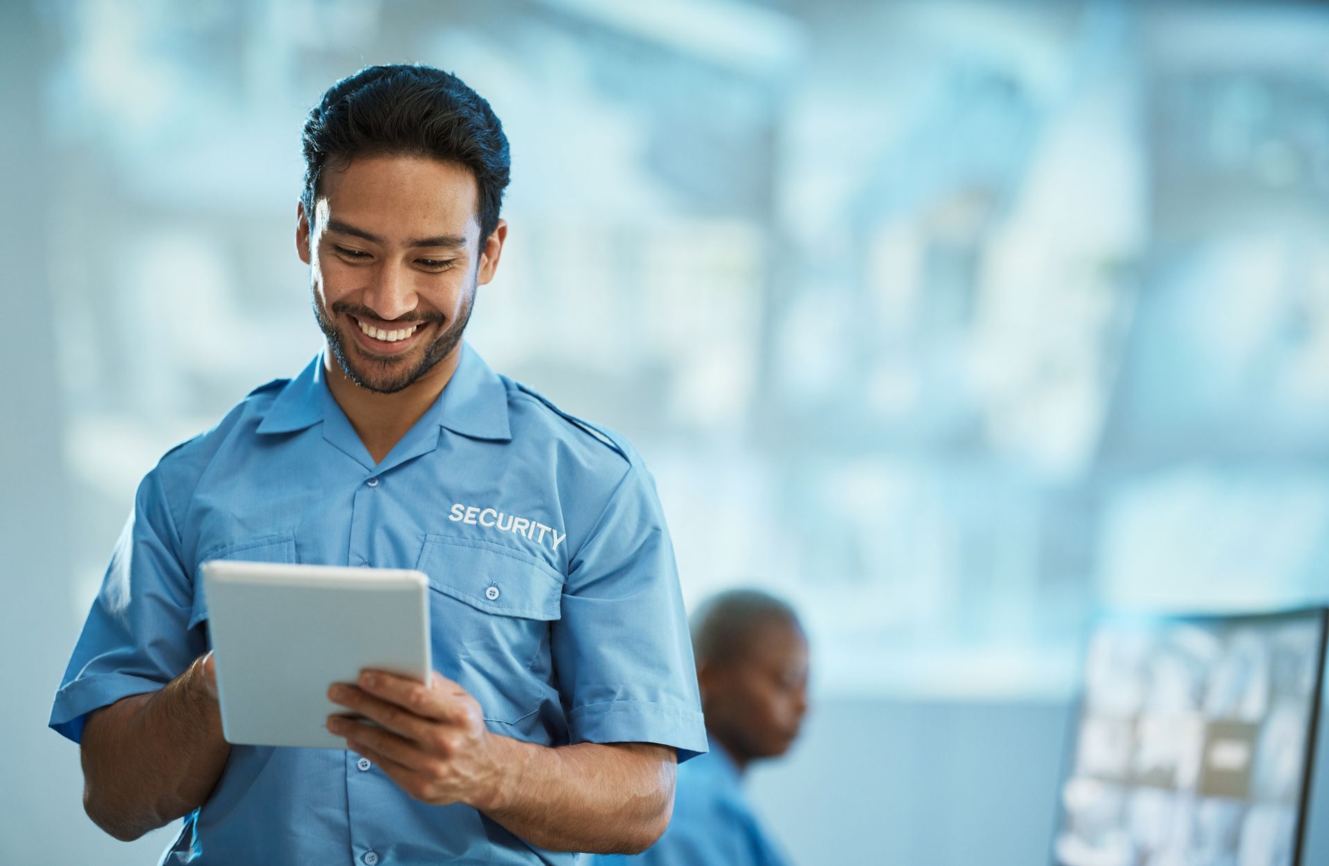 A security guard is smiling while using a tablet computer.