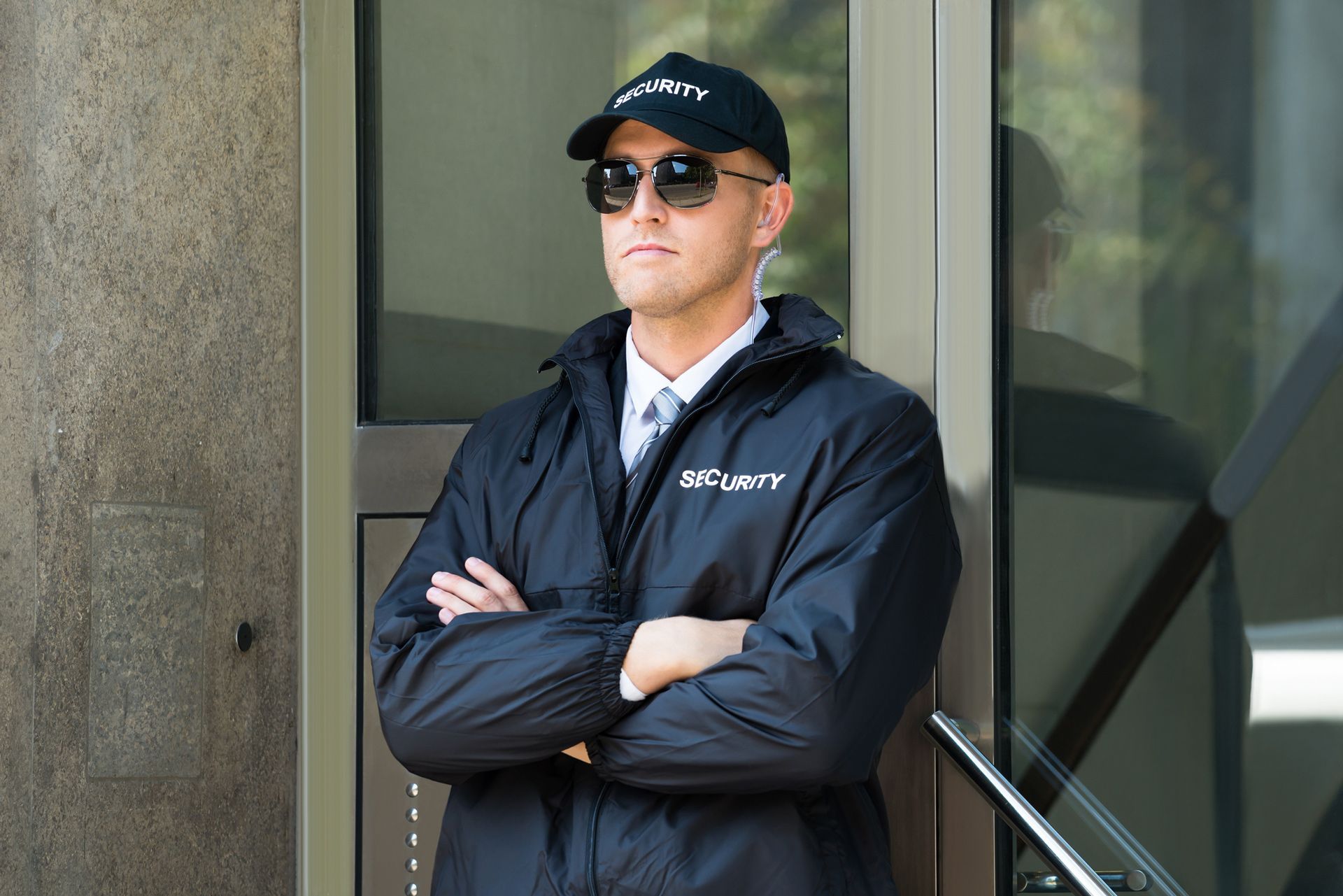 A security guard is standing in front of a door with his arms crossed.