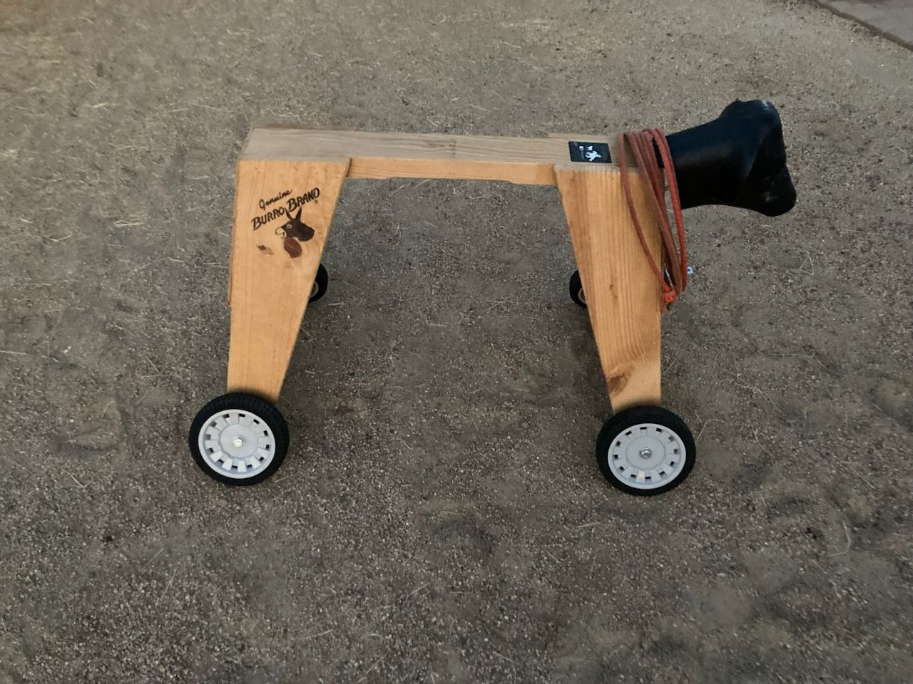 A wooden roping dummy with a black head and wheels sits on a dirt surface.