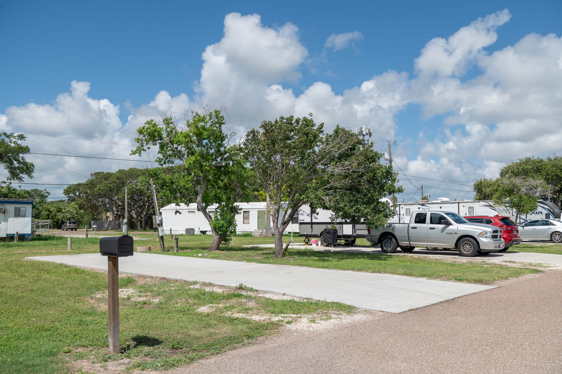 Rural driveway with parked cars, a mailbox, and small homes under a partly cloudy sky