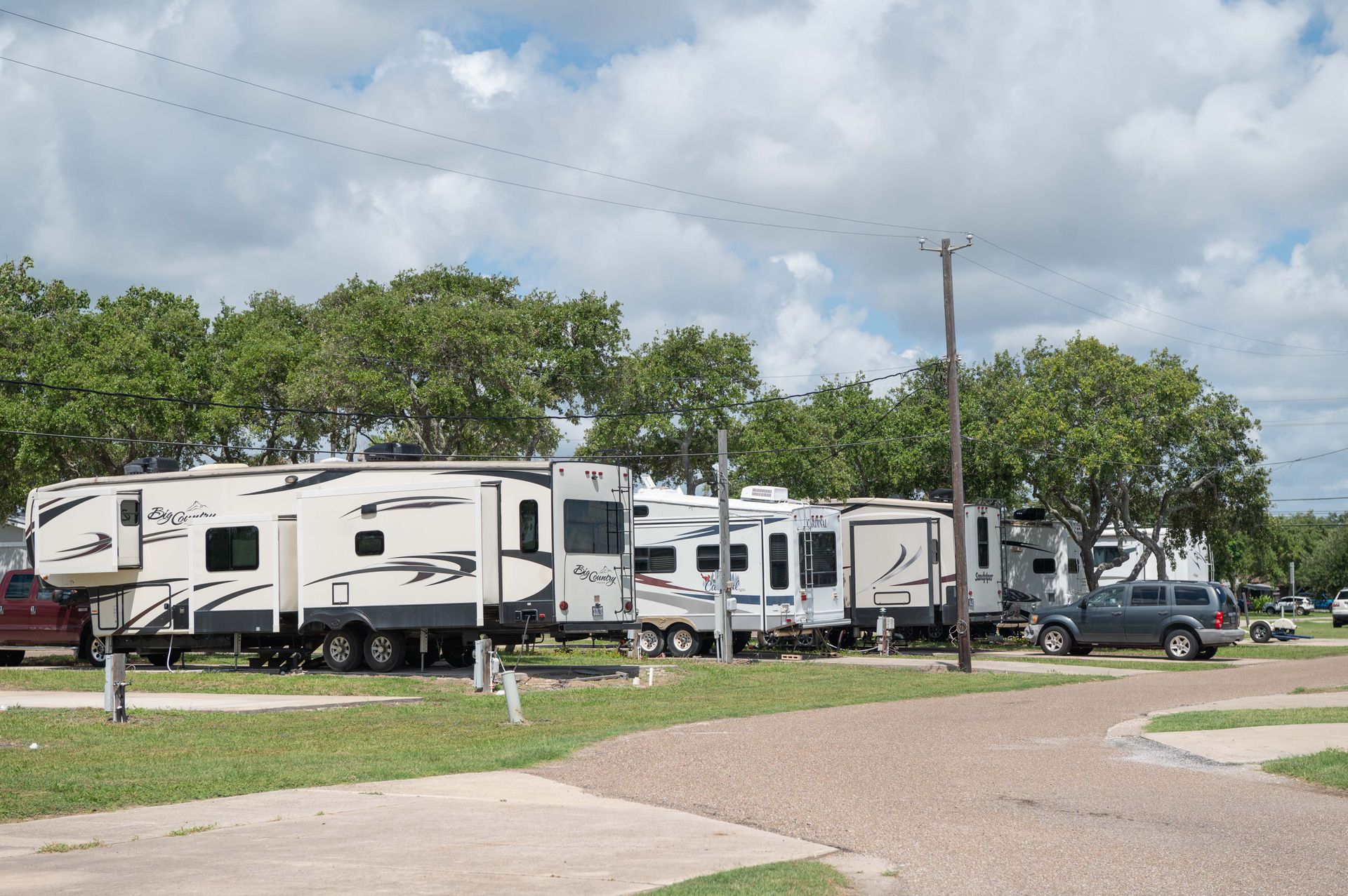 Row of white RV trailers parked along a grassy campground under a cloudy sky