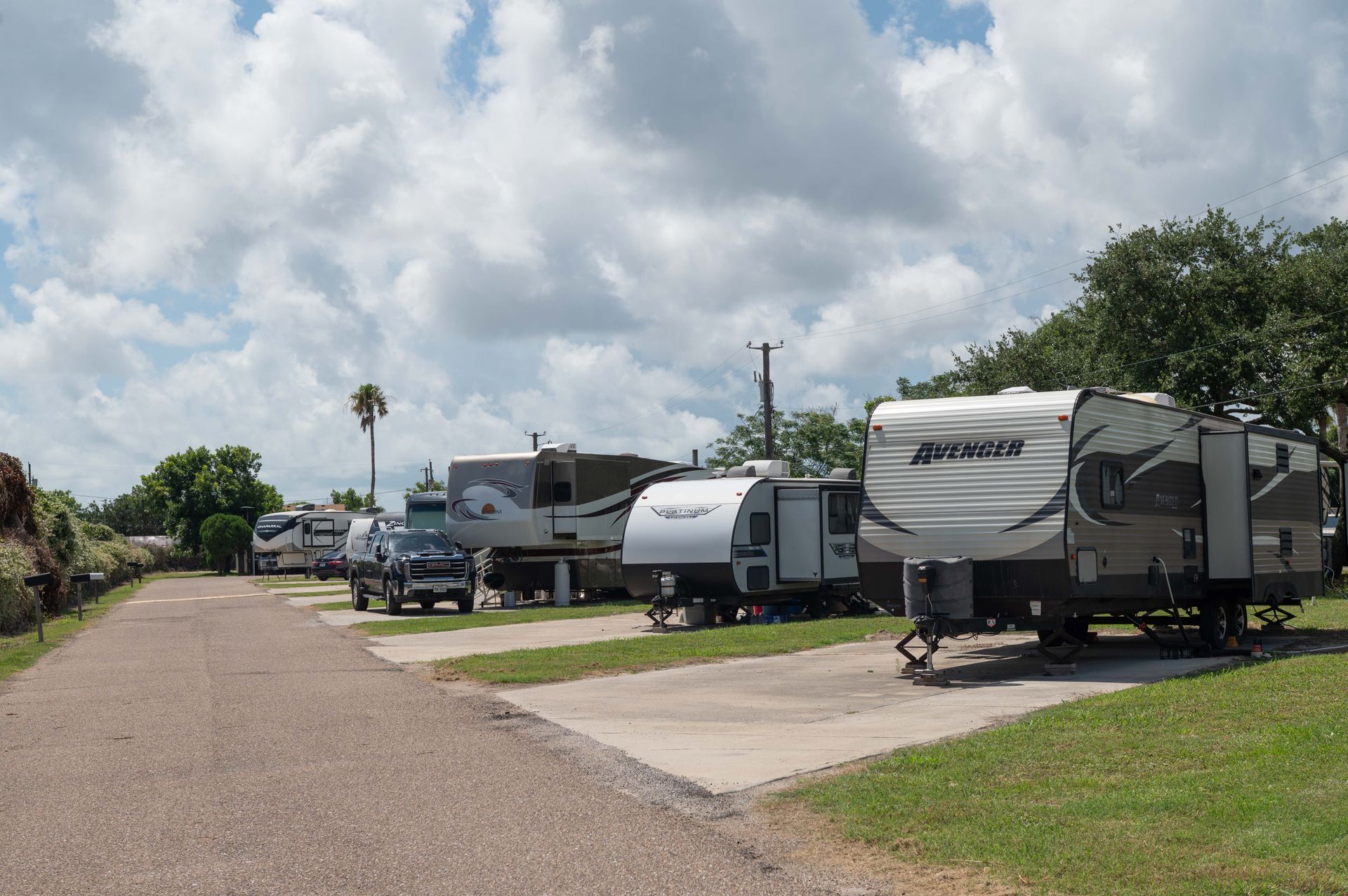 RVs and trailers parked along a gravel road at a campground under a cloudy sky
