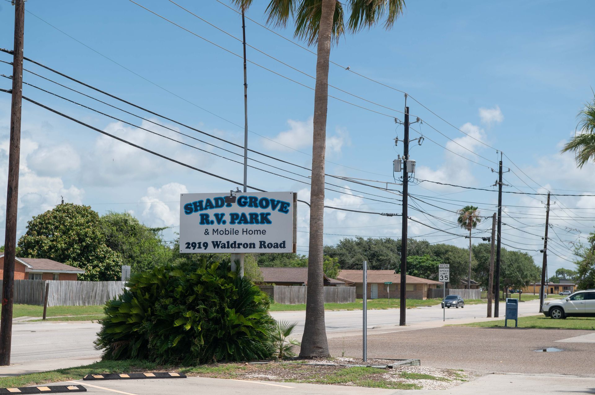 Sign for Shady Grove RV Park beside a roadside, with palm trees and a clear blue sky