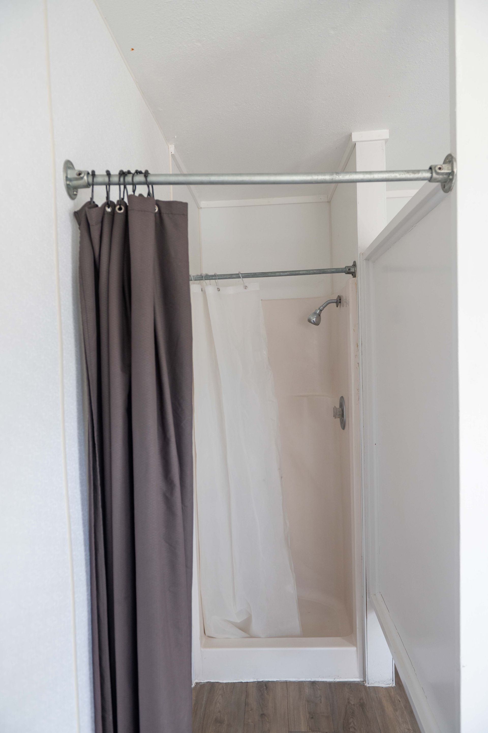 Small bathroom shower with gray curtain and clear liner on a white curtain rod.