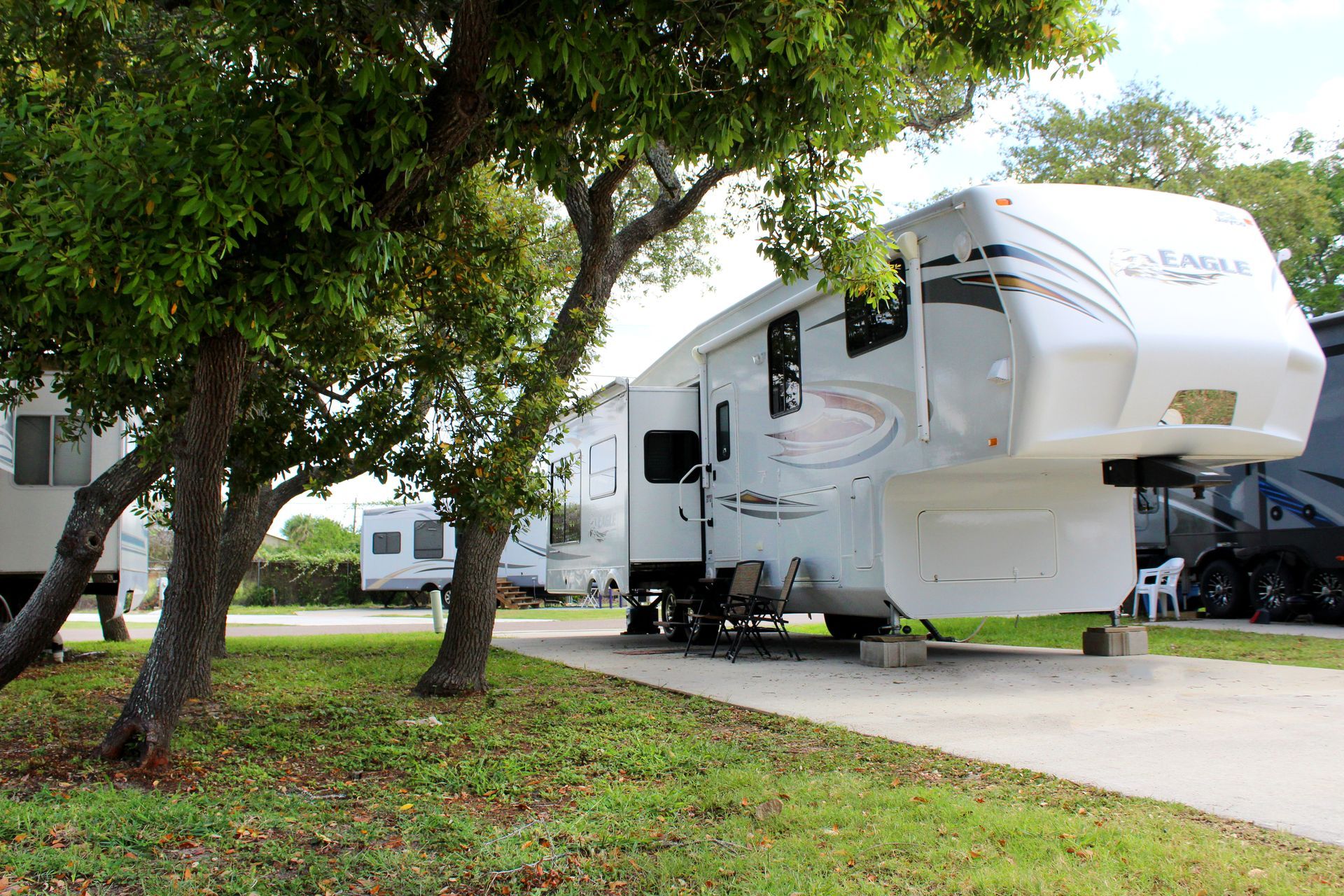 Large white RV parked on a driveway beside trees in a grassy campground area