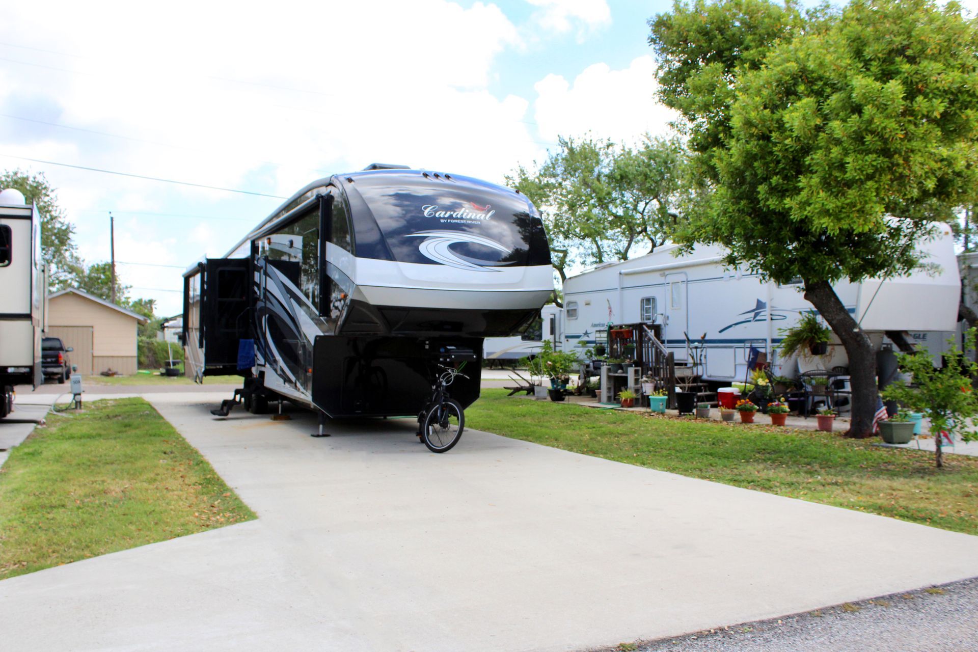Large black RV parked on a concrete driveway beside a house and trees