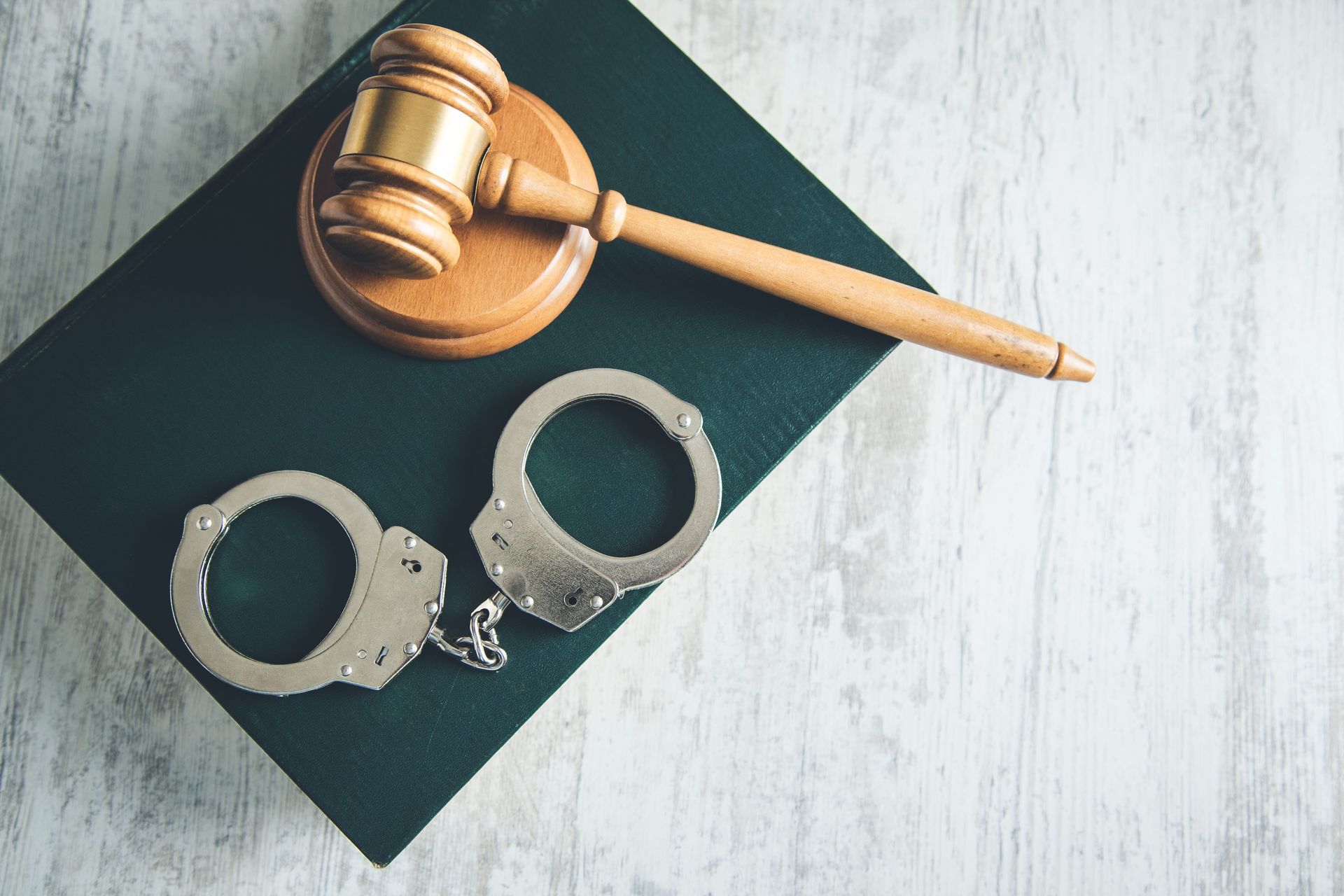 Wooden judge’s gavel beside open handcuffs on a dark book or folder, on a light surface.